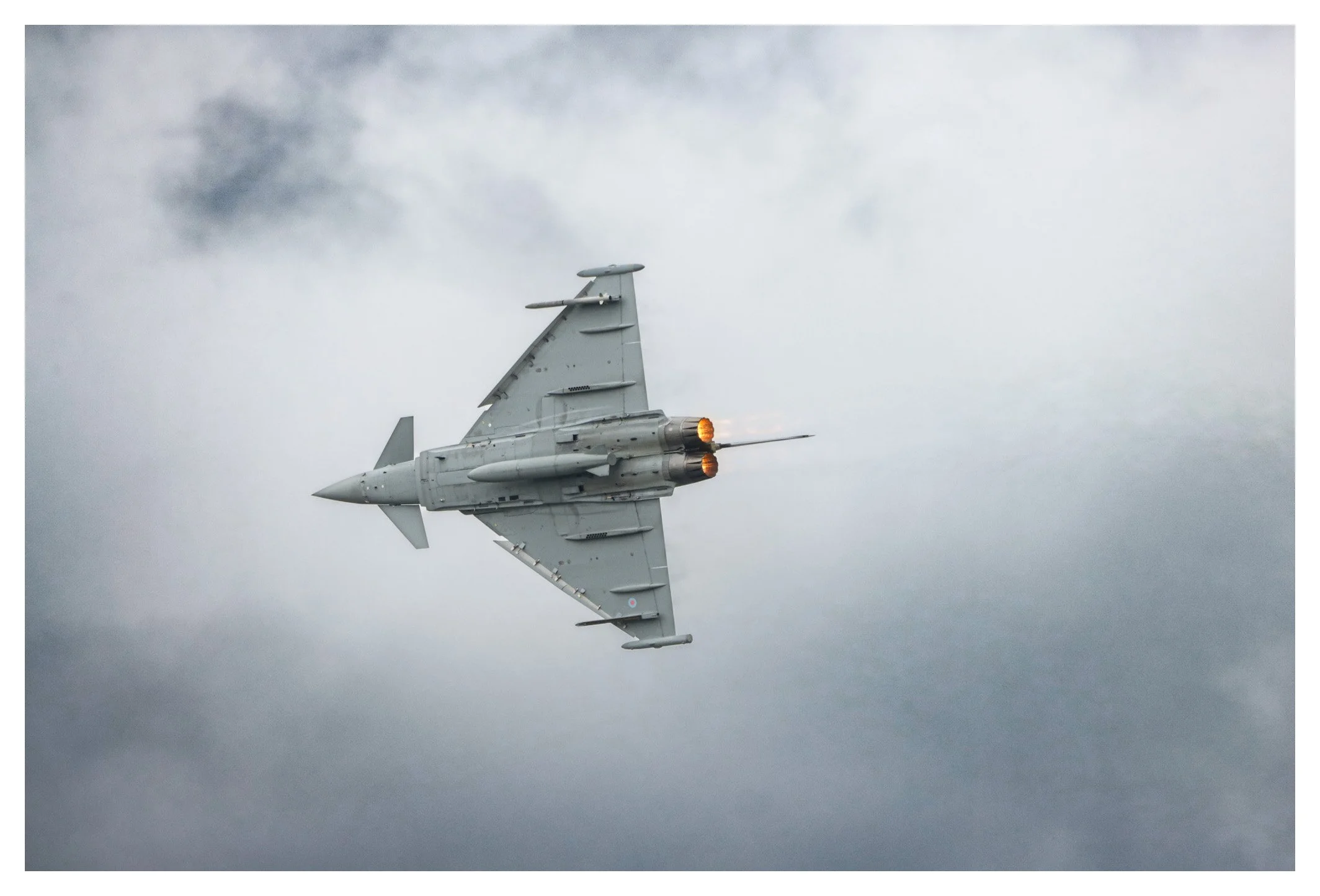 A fighter jet flying through cloudy skies with afterburners ignited.