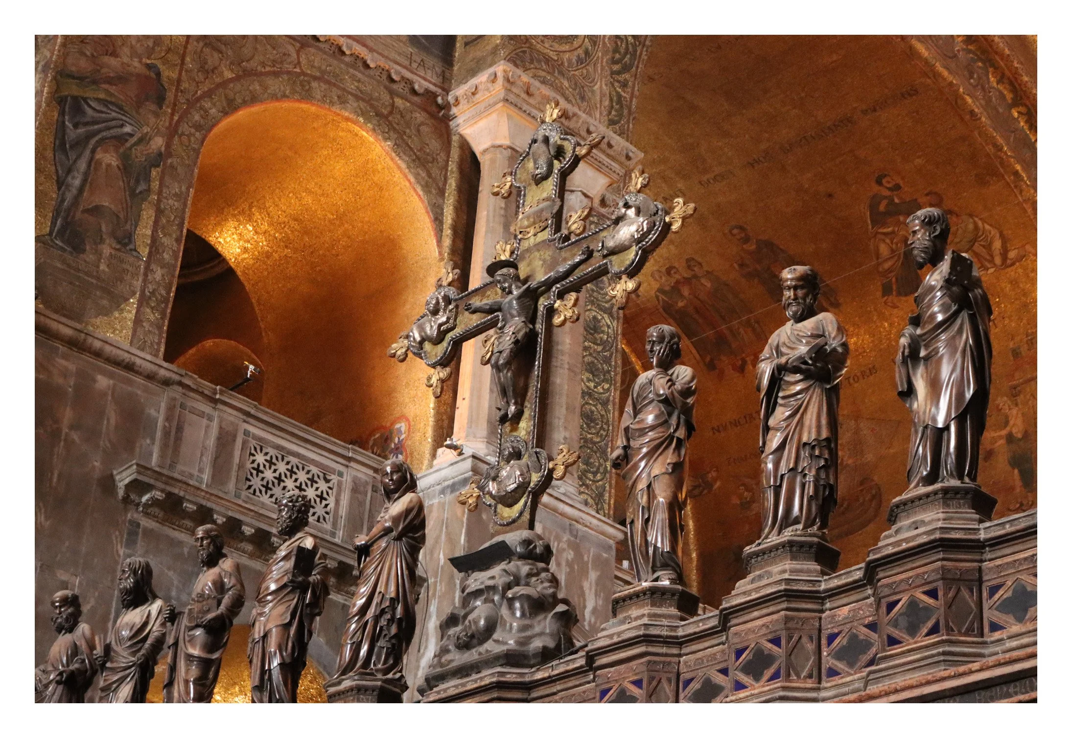 Interior of a cathedral or church with religious statues on a ledge, showcasing a crucifix with Jesus on the cross, and a golden ceiling in the background.