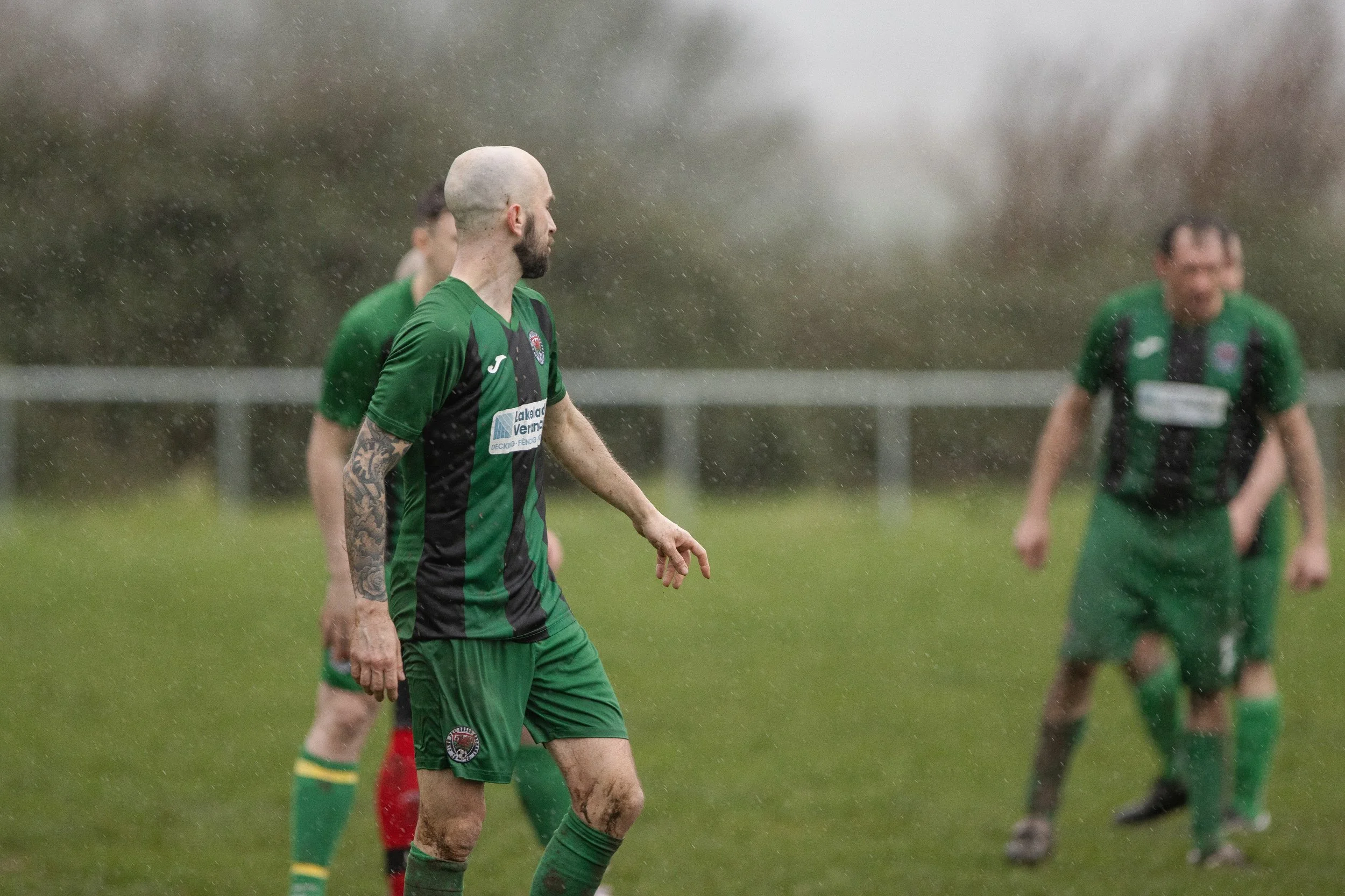 Soccer players in green uniforms on a rainy field during a match.