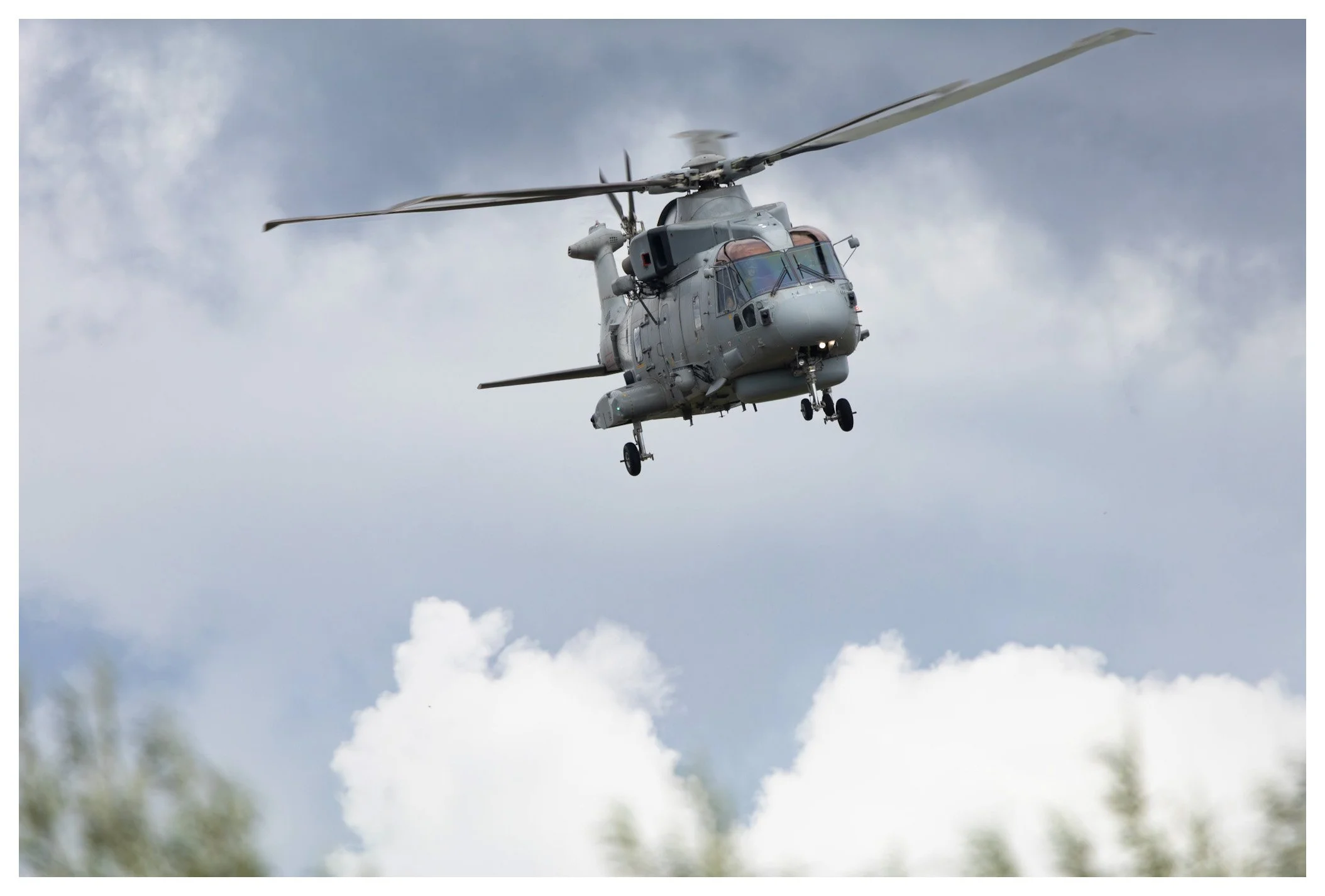 A military helicopter flying in the sky with clouds in the background.