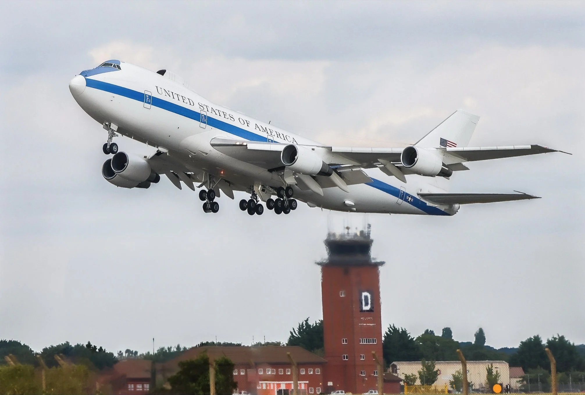 Air Force One aircraft landing at an airport, passing low over a control tower and buildings.
