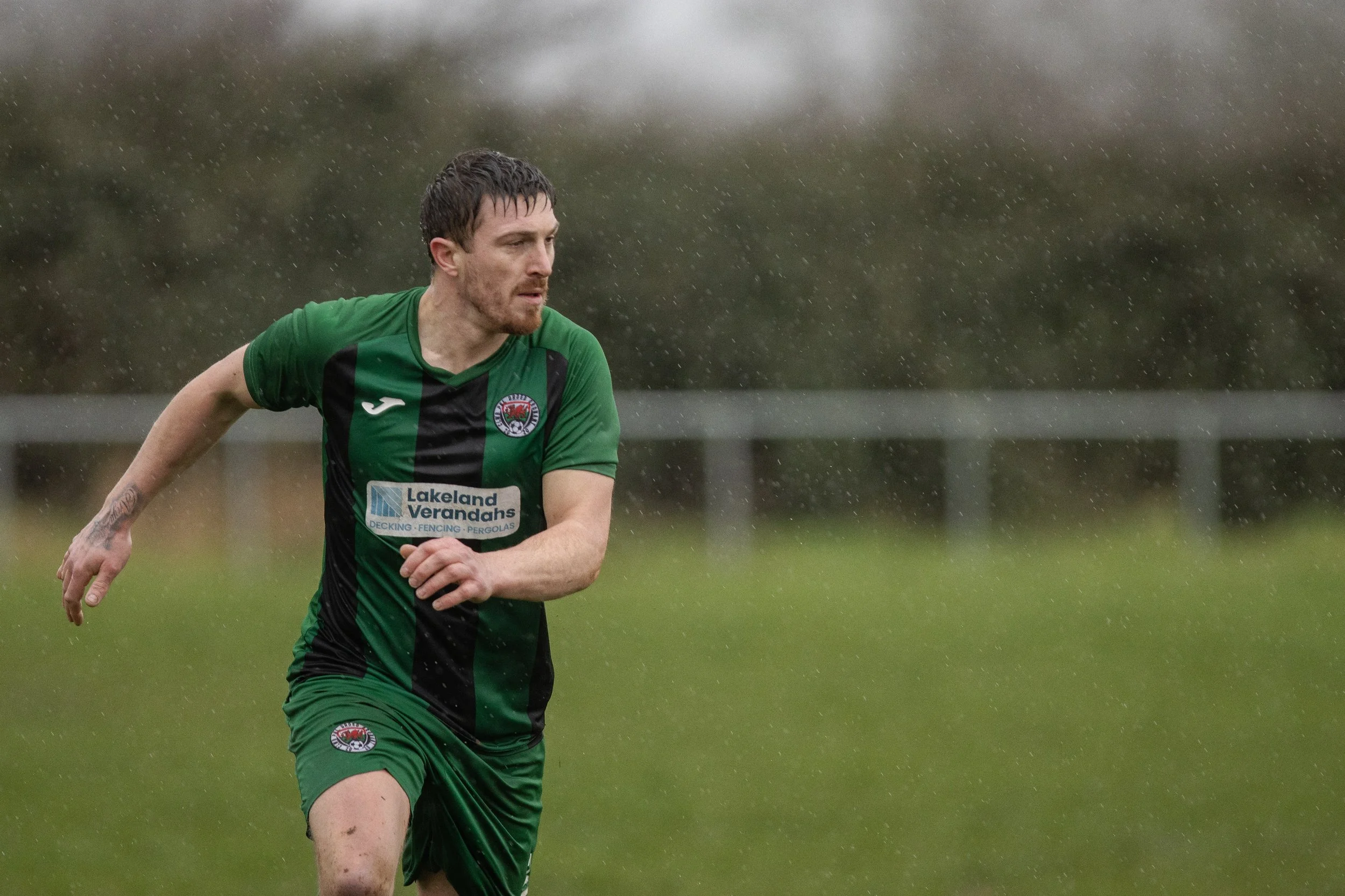 A man in a green and black sports uniform running outdoors on a rainy day.