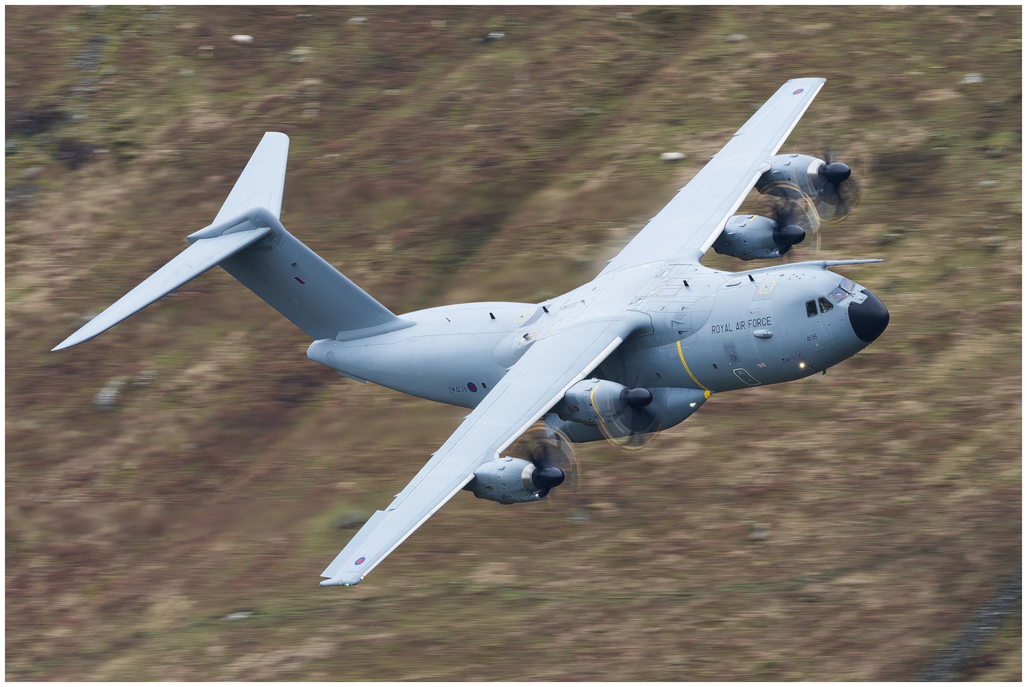 A Royal Air Force aircraft flying low over a grassy terrain with a blurred background, showing its side and underside.