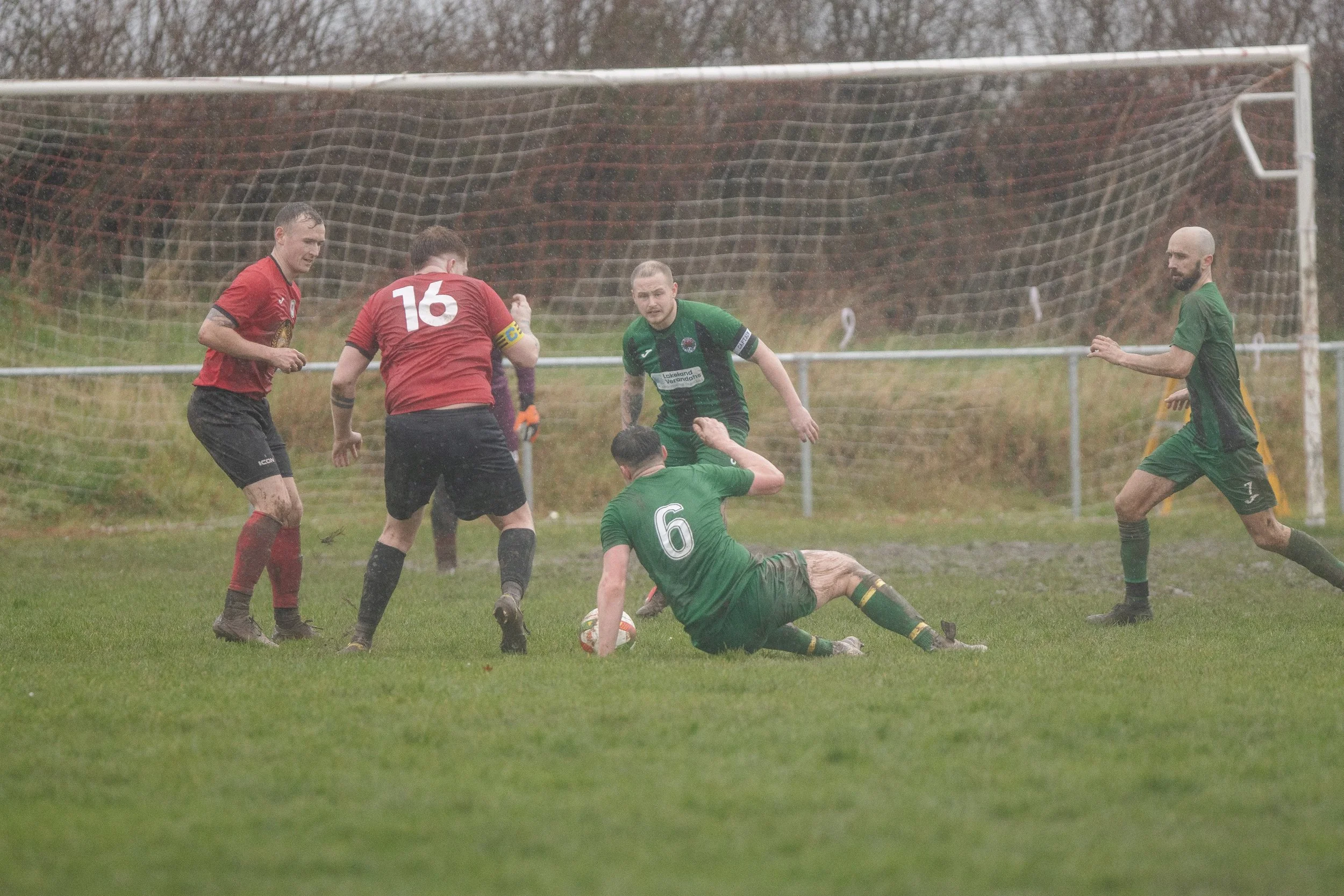 Soccer players in green and red jerseys competing for the ball during a match on a grassy field.