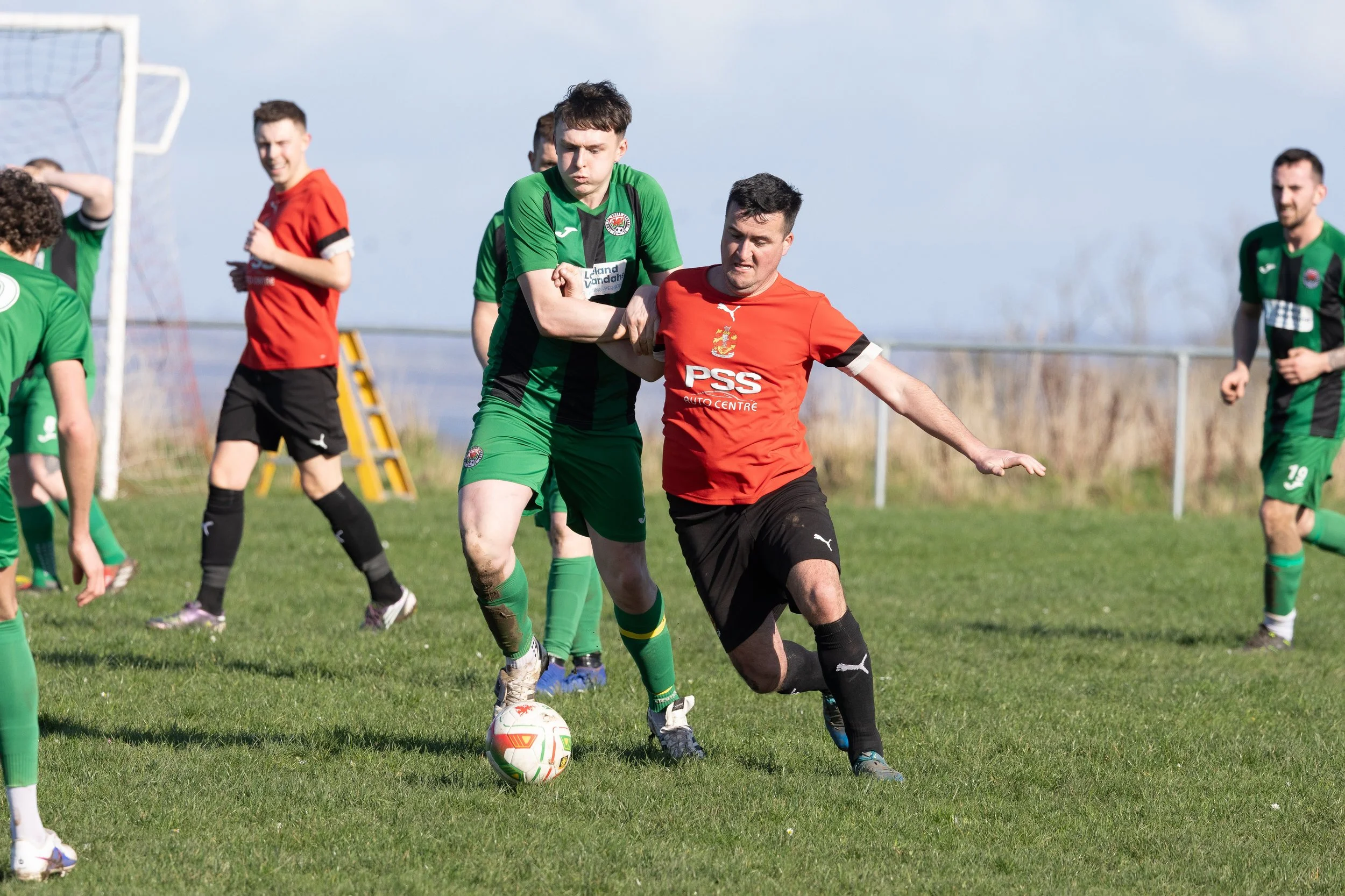 Soccer players in green and red jerseys compete for the ball on a grassy field during a match.