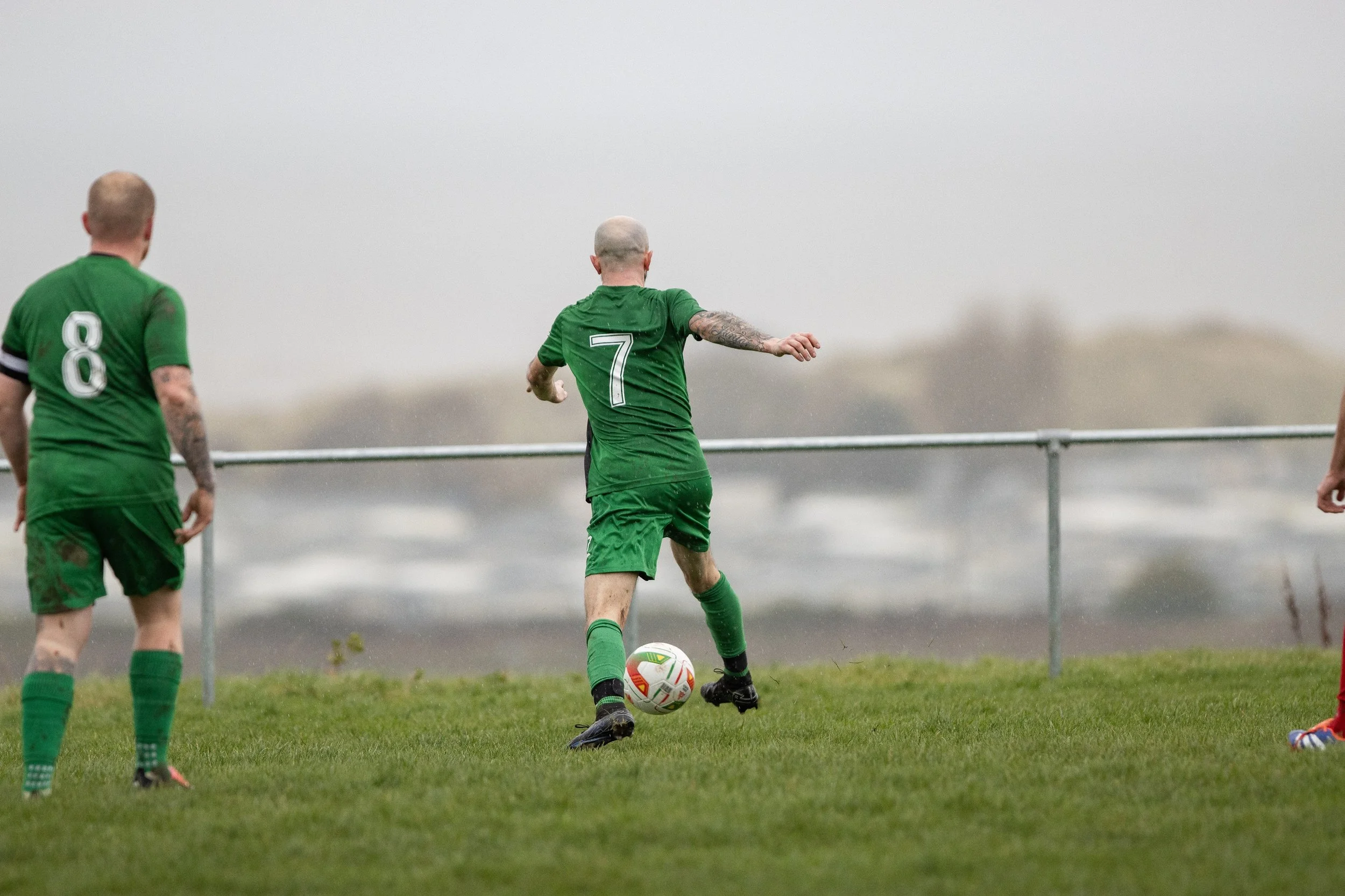 Soccer players in green jerseys on a field, with one player preparing to kick the ball.