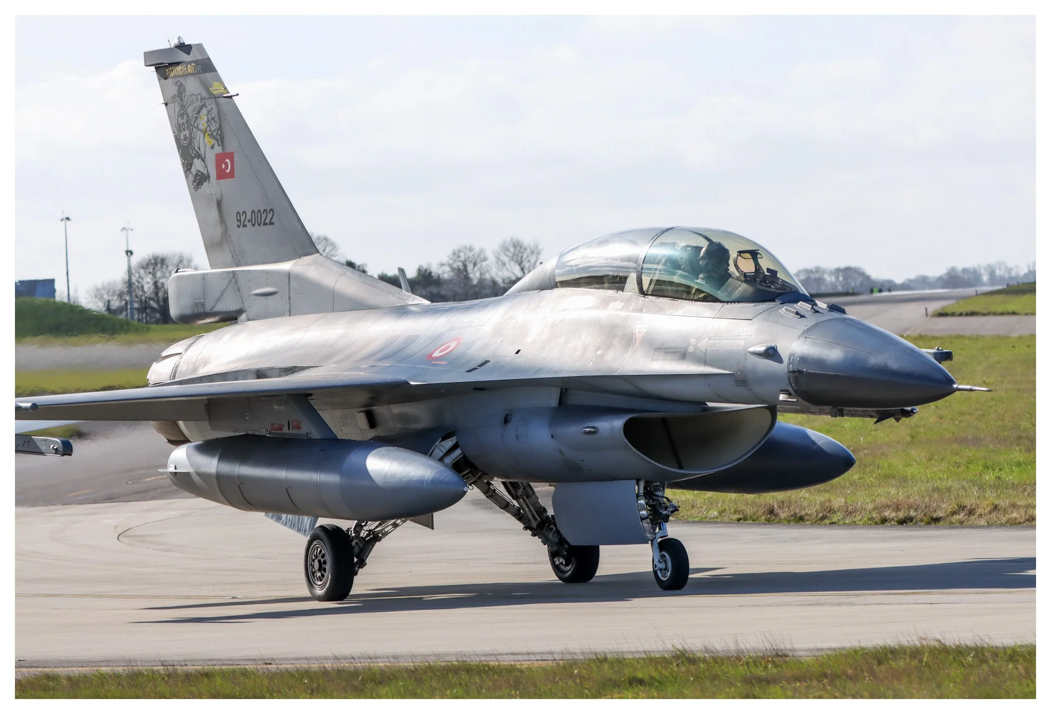 A fighter jet taxiing on a runway, with a pilot visible through the cockpit.