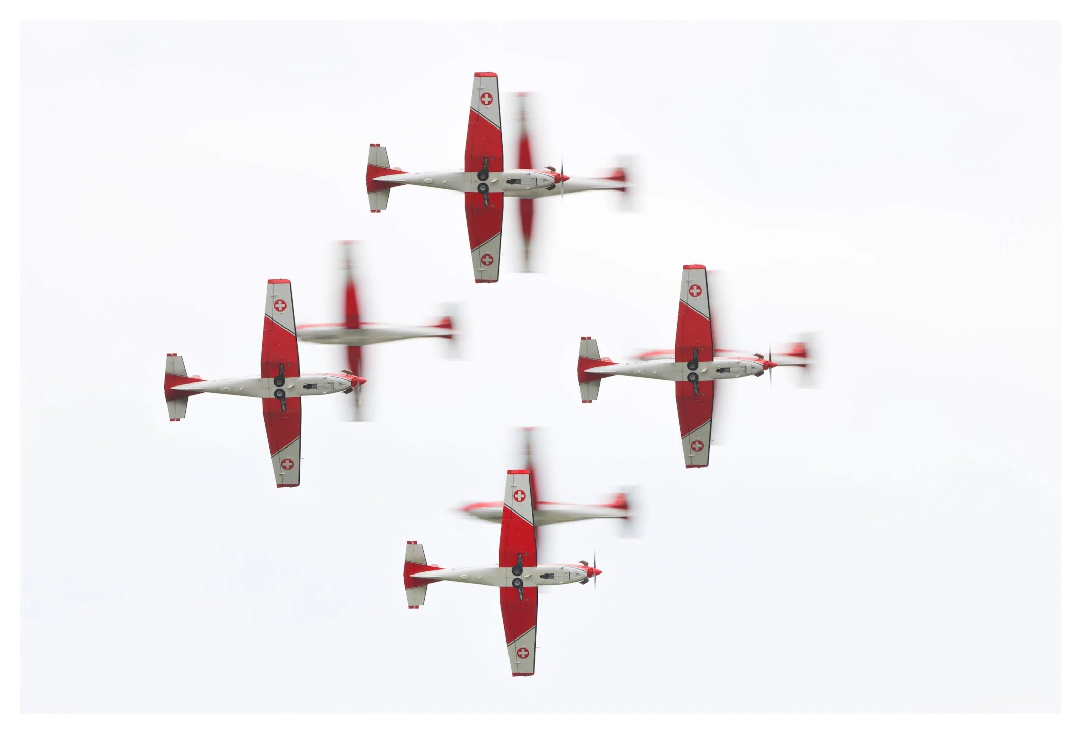 Five white and red aircraft with Swiss flags flying in a formation against a cloudy sky.