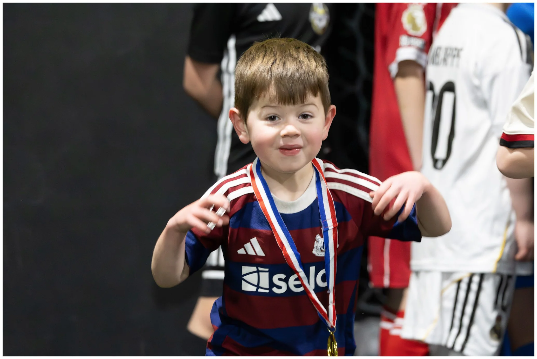Young boy in a soccer jersey with a medal around his neck, celebrating a victory at a sports event.