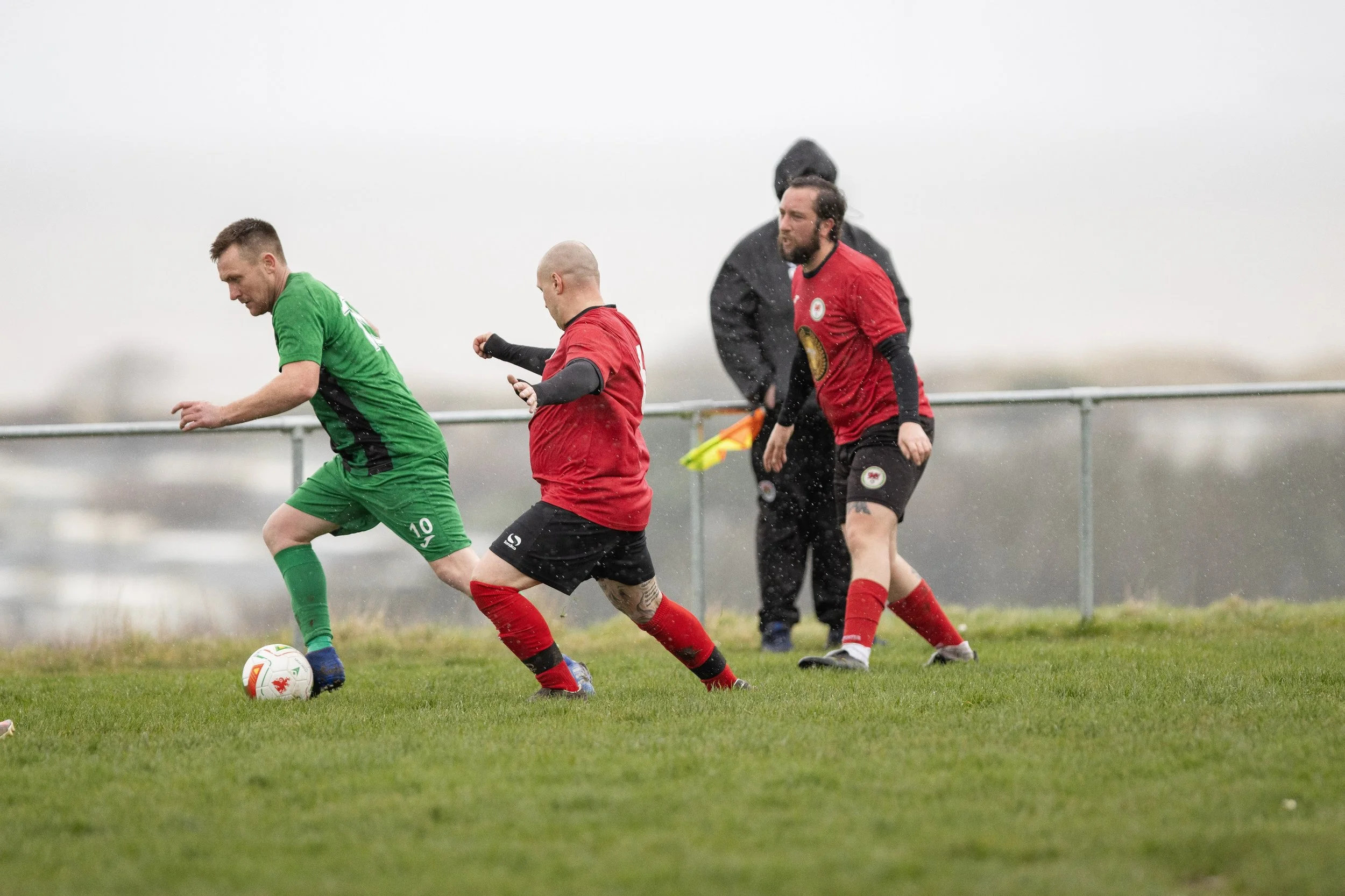 Soccer players in red and green uniforms on a rain-soaked field competing for the ball.