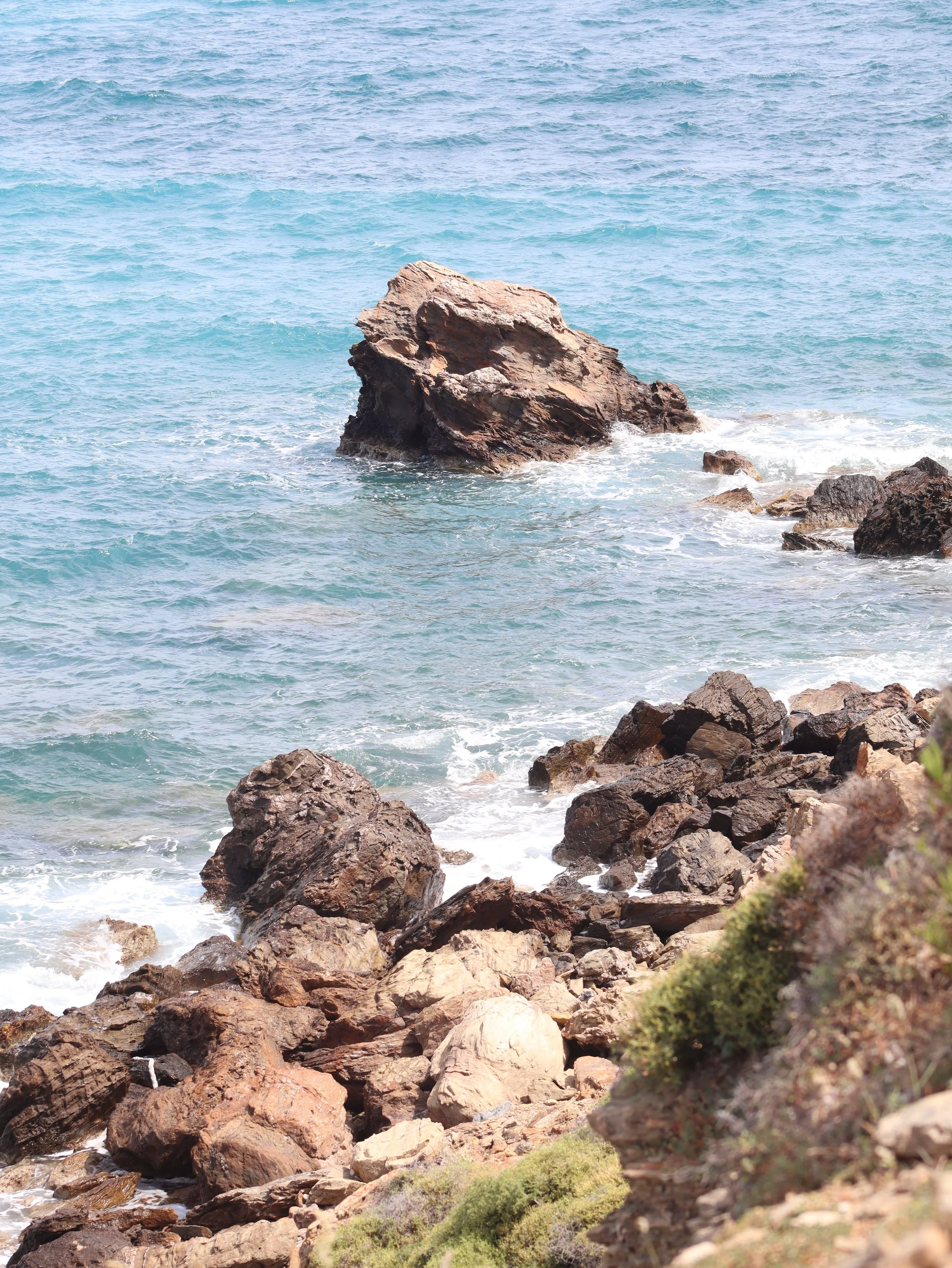 Rocky coastline with large rocks and boulders, ocean waves, and turquoise water.