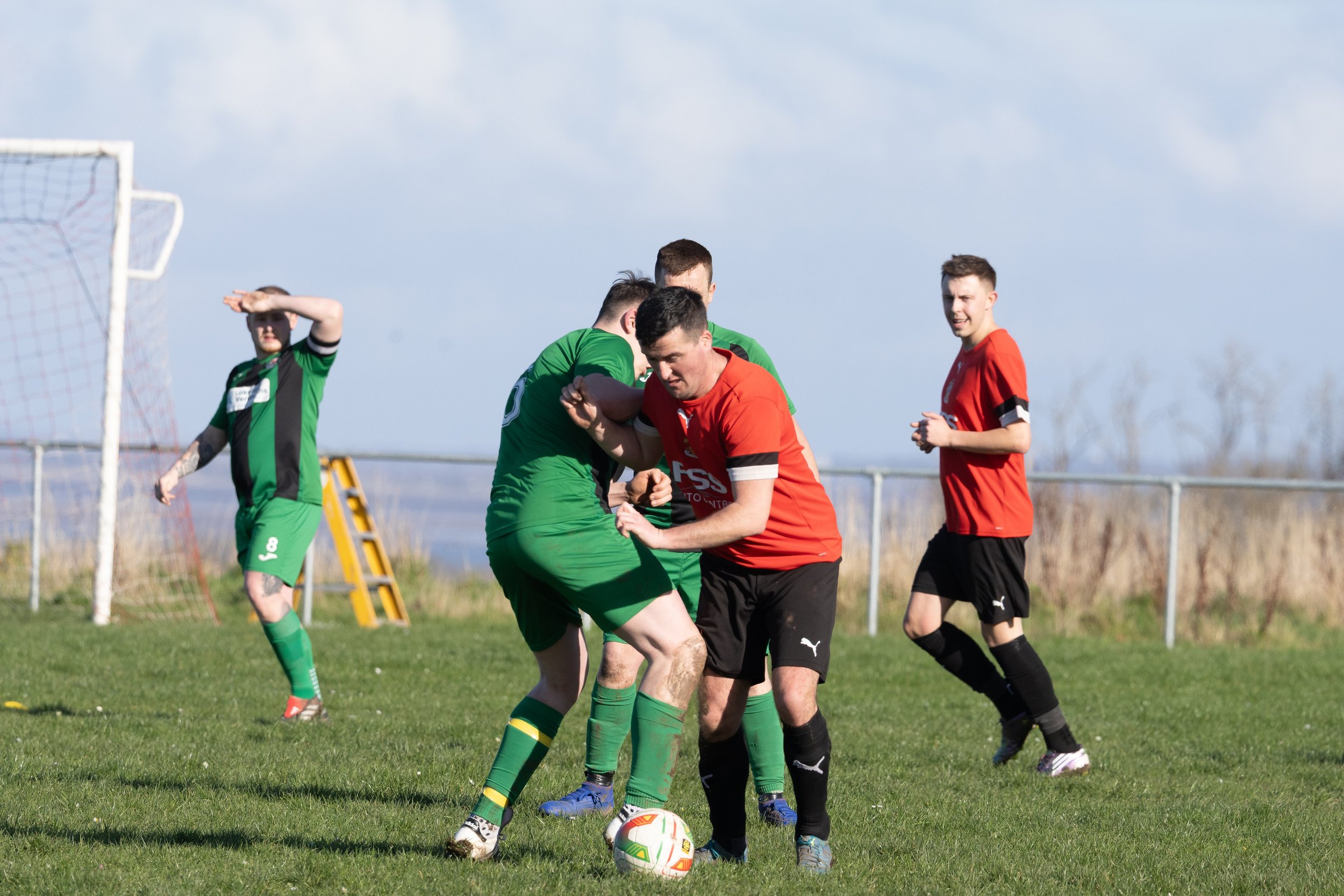Soccer players in green and red jerseys competing for the ball on a grassy field during a match.