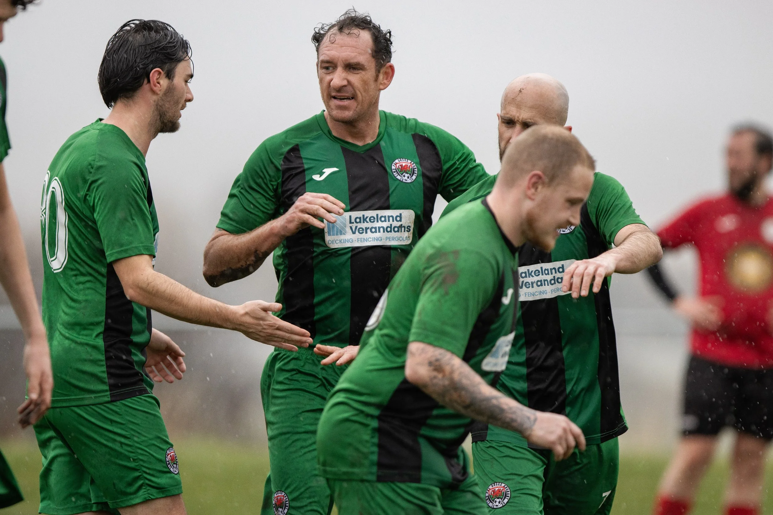 Football players in green and black uniforms on a field, during a game in rainy weather.