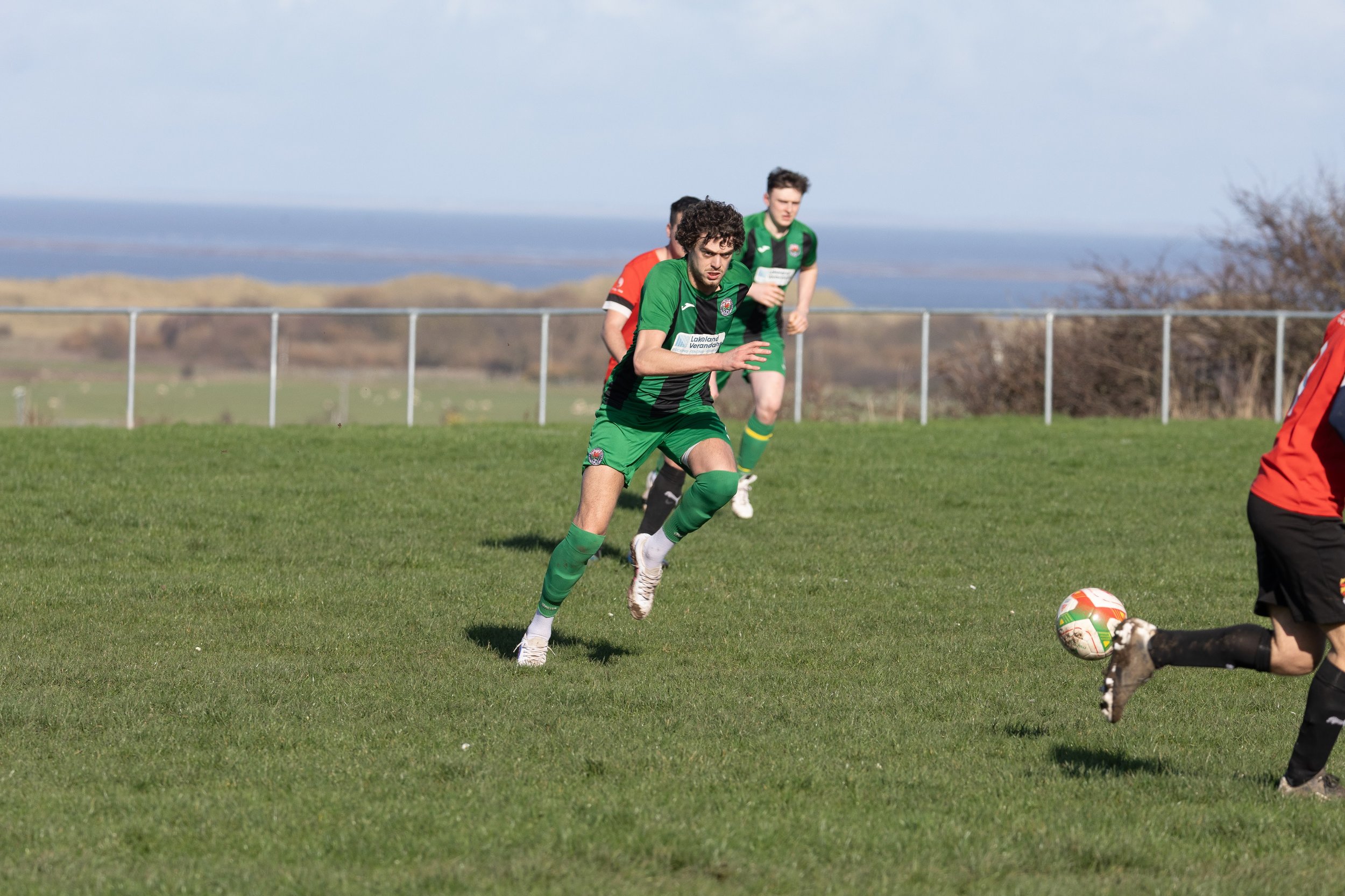 Soccer players in green and red uniforms running on a grassy field during a match.
