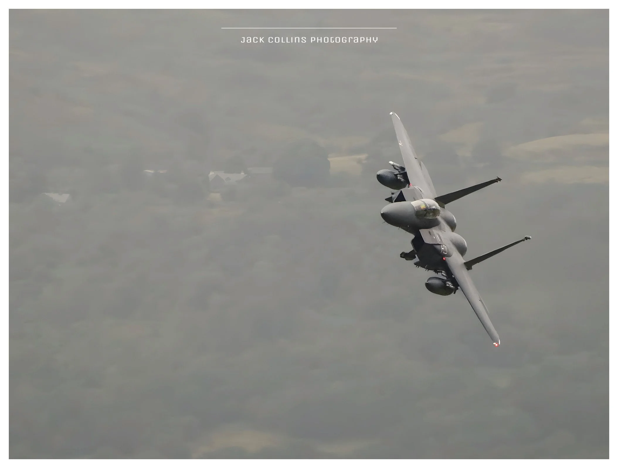 An F-15 fighter jet flying through a cloudy sky with a reflection visible in a glass window.