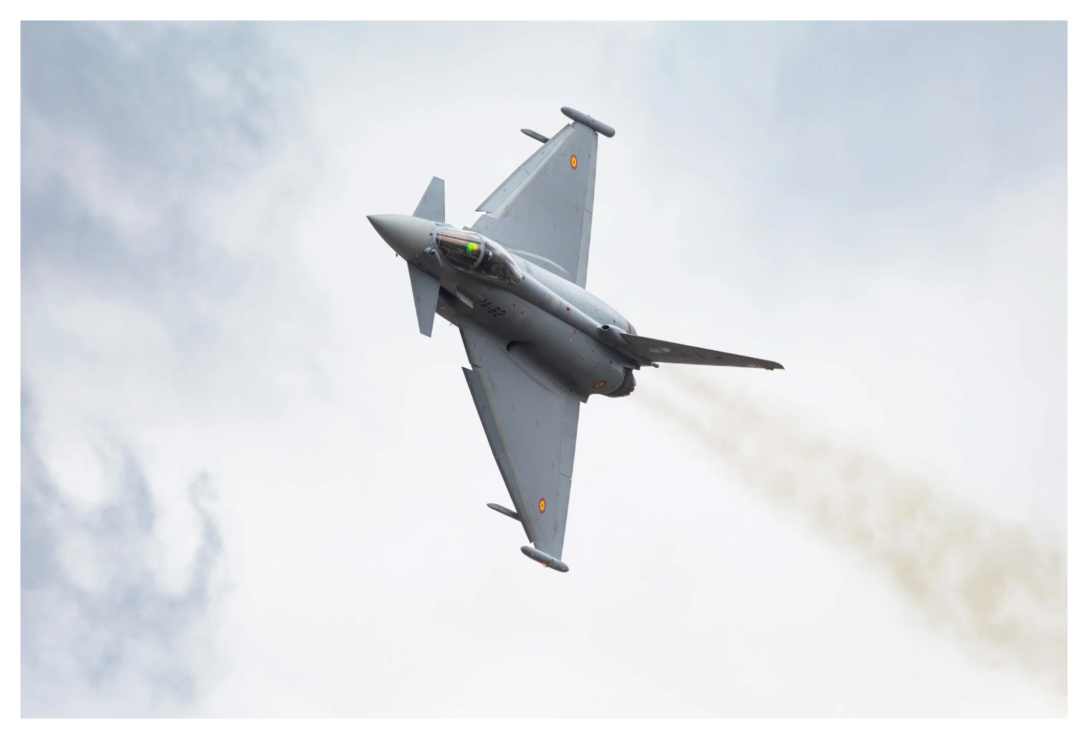 A military fighter jet flying through the sky with a trail of smoke behind it.