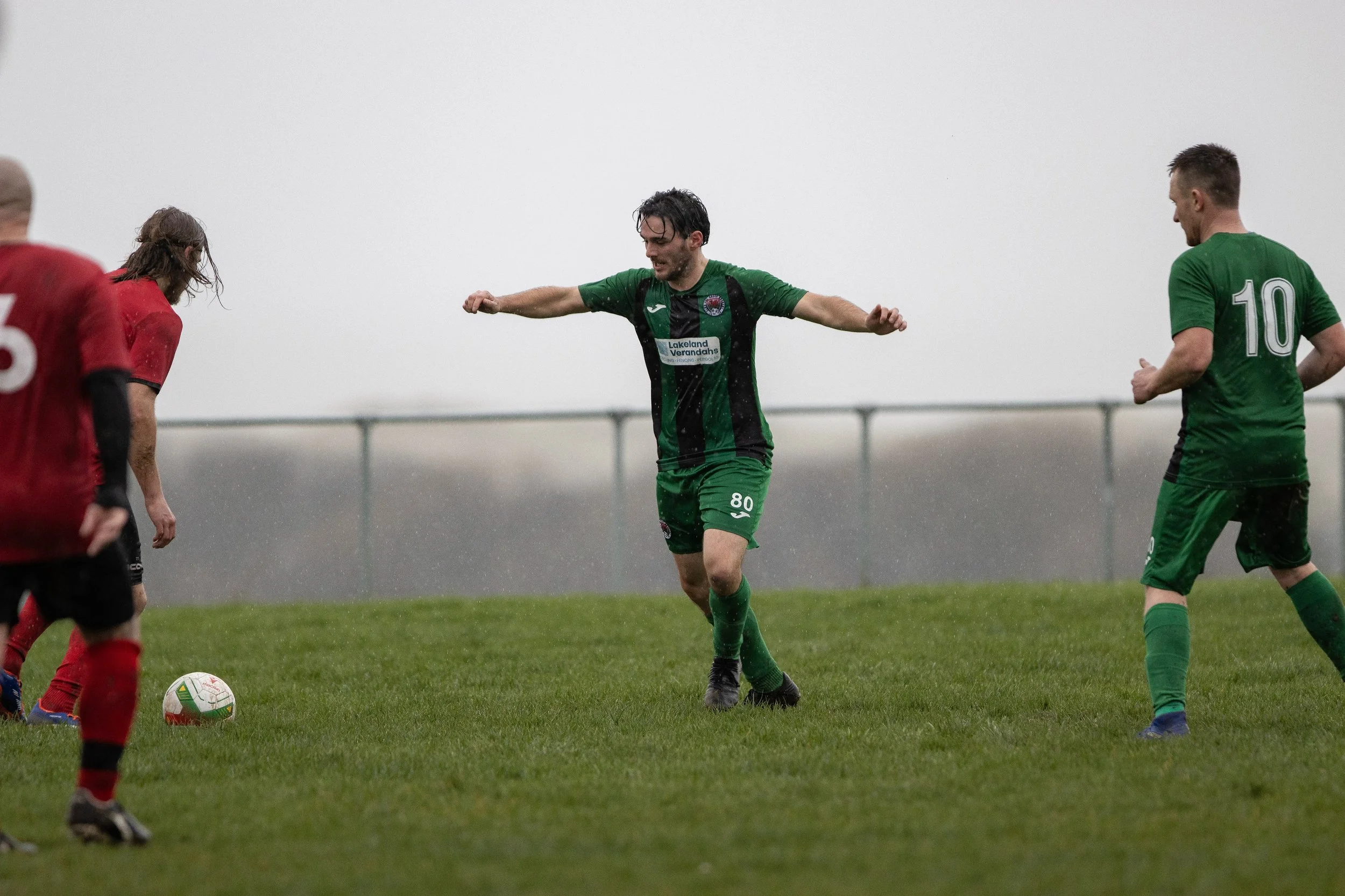 Soccer players in green and red jerseys on a rainy field during a game.