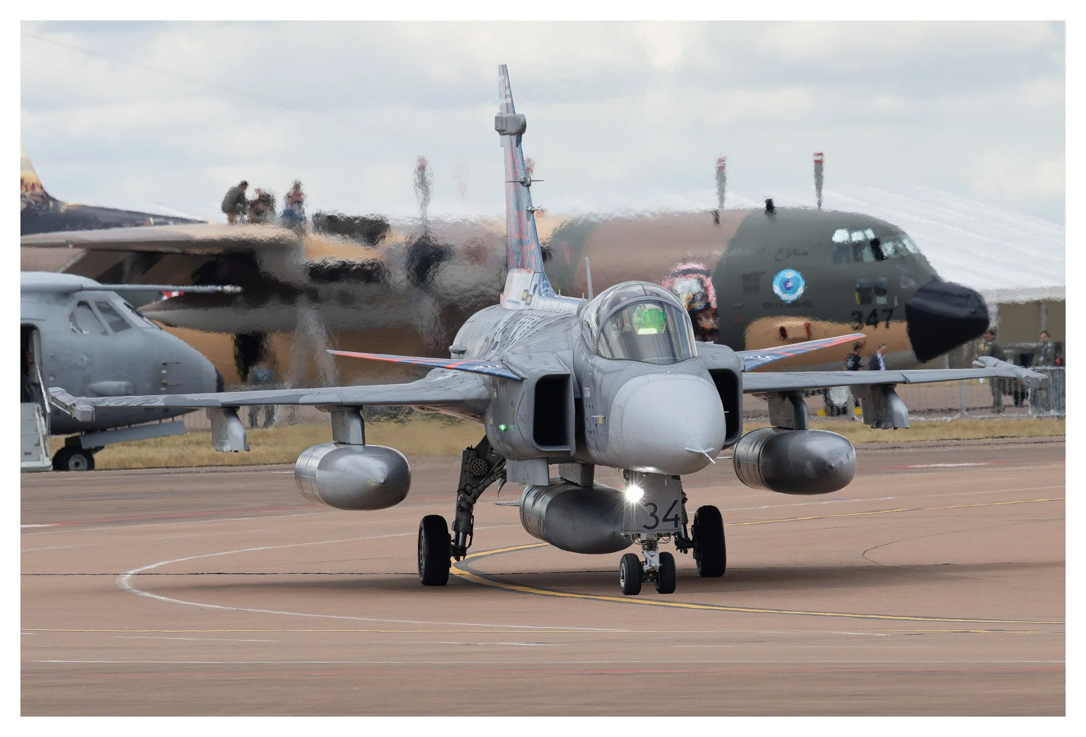 Military fighter jet taxiing on the runway with other military aircraft and personnel in the background