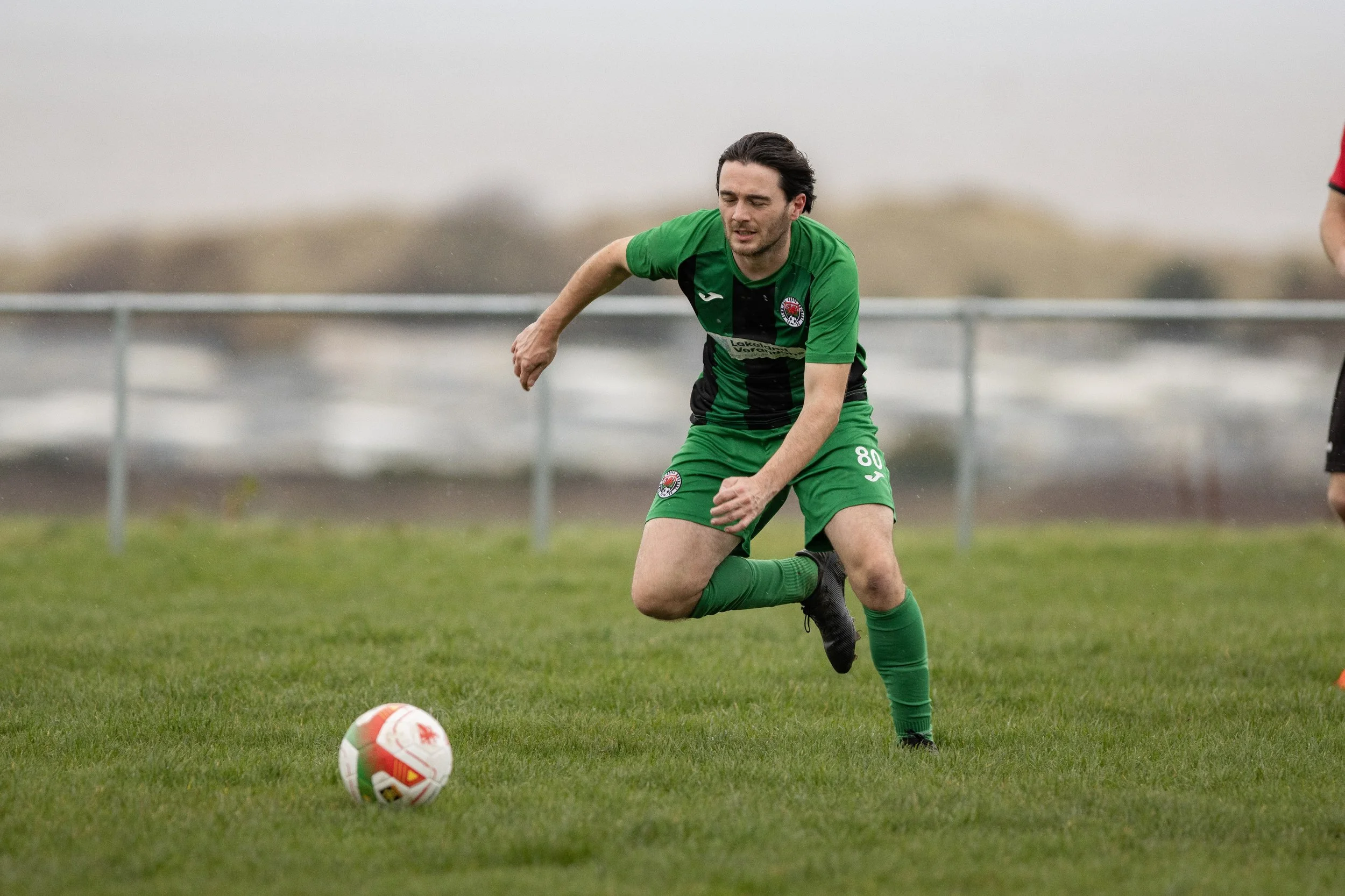 A soccer player in a green and black uniform running on a grassy field, about to kick a soccer ball.