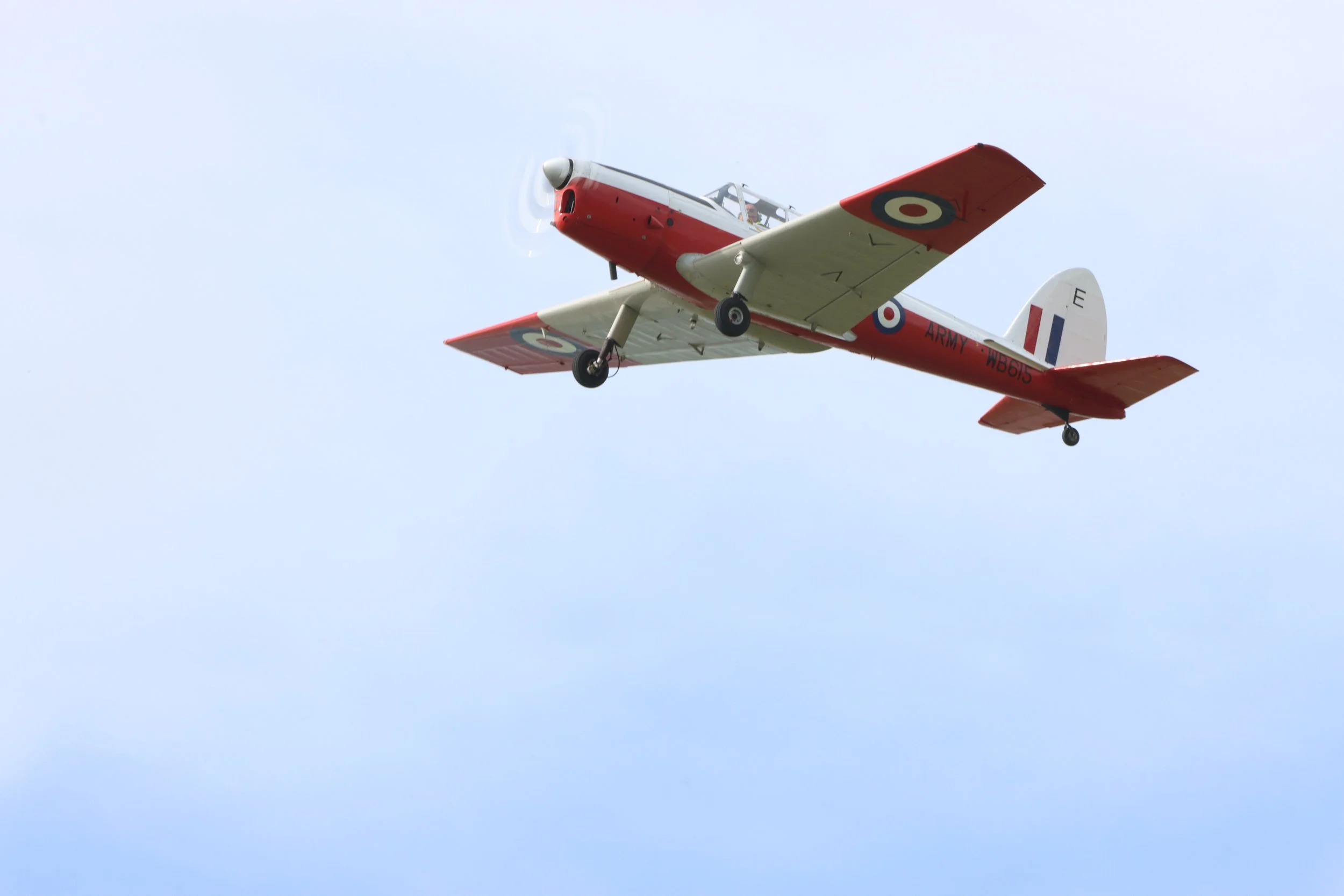 A vintage red and white airplane flying in a clear blue sky.