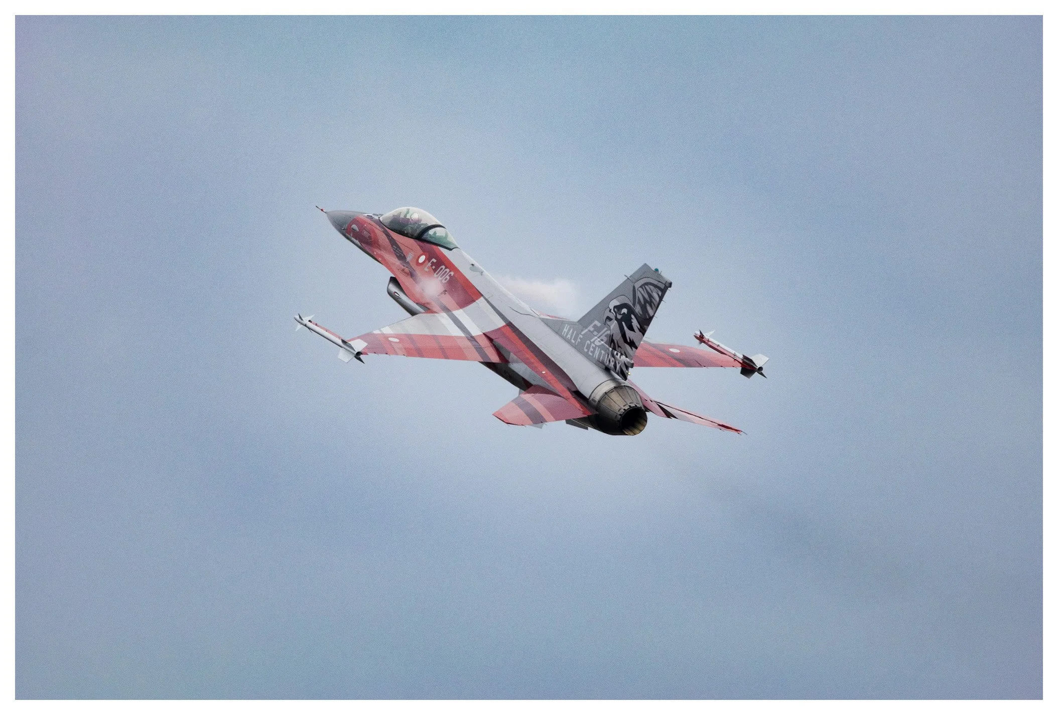An aircraft with a red, white, and grey striped design and a black and white eagle logo on the tail, flying through the sky.