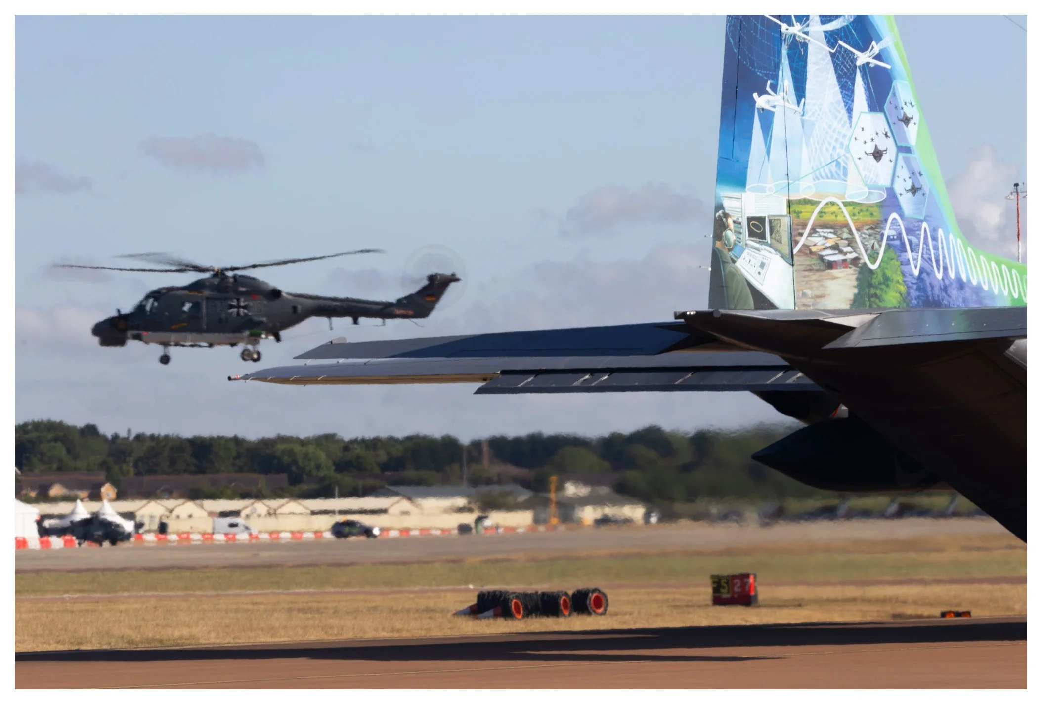 An aircraft with a colorful design on the tail, taking off with a helicopter in the background on a runway.