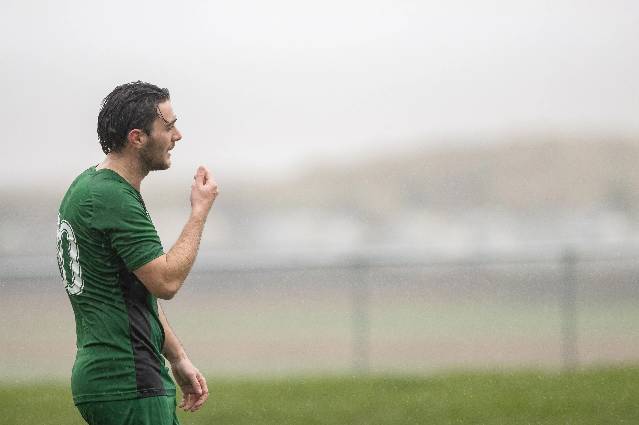 A man in a green sports jersey with the number 10 on the back, celebrating with his fist raised in the rain on a soccer field.