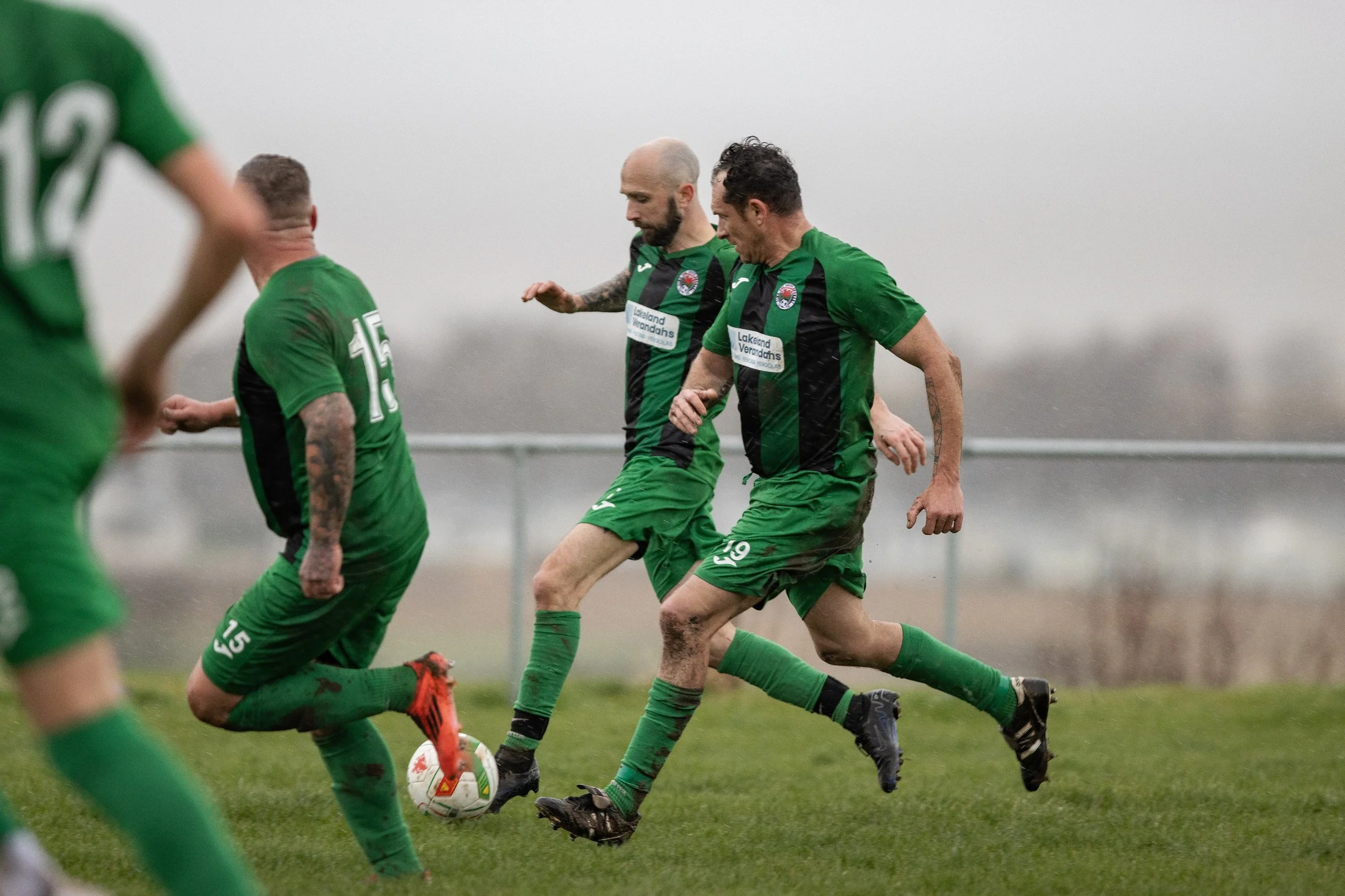 Soccer players in green jerseys competing for the ball on a rainy field during a game.