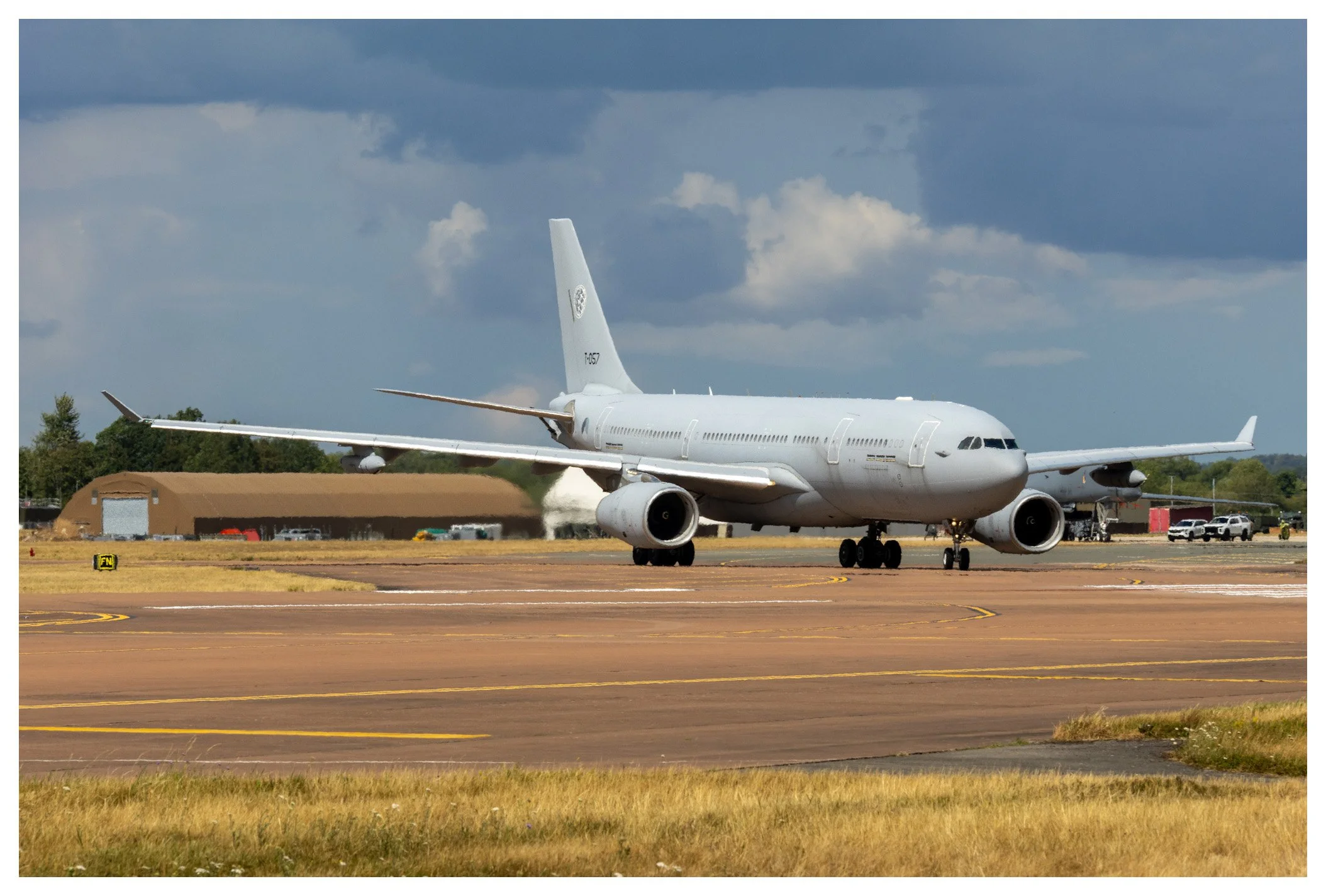 A large white commercial airplane on an airport runway with dark clouds in the sky and airport buildings in the background.