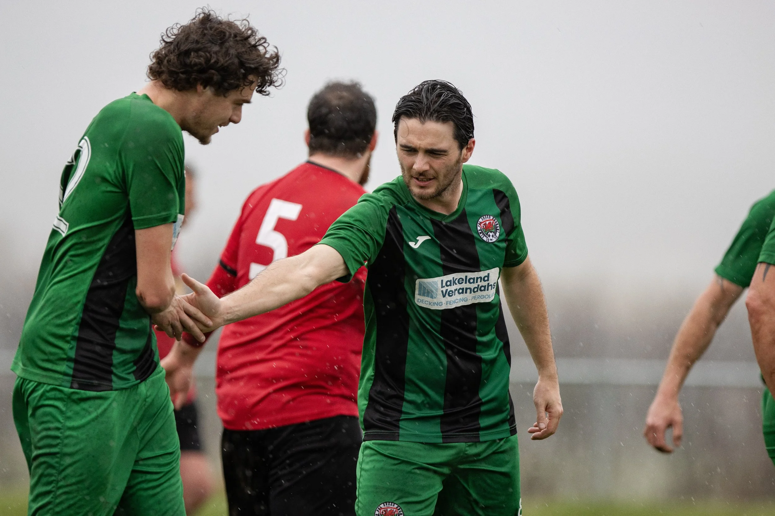 Soccer players in green and red uniforms on a rainy field, with one player shaking hands with another
