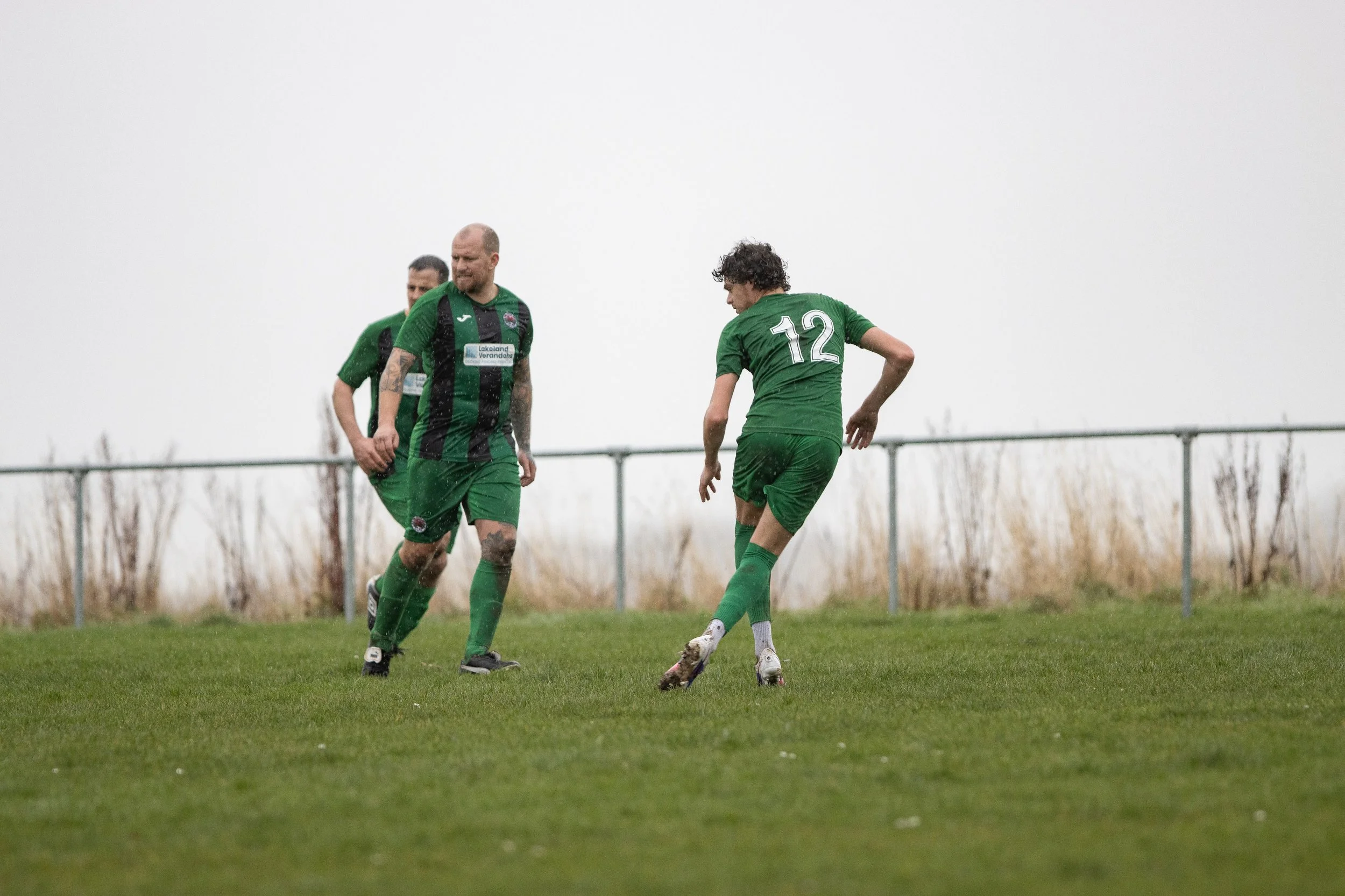 Soccer players in green uniforms celebrating on field with overcast sky.