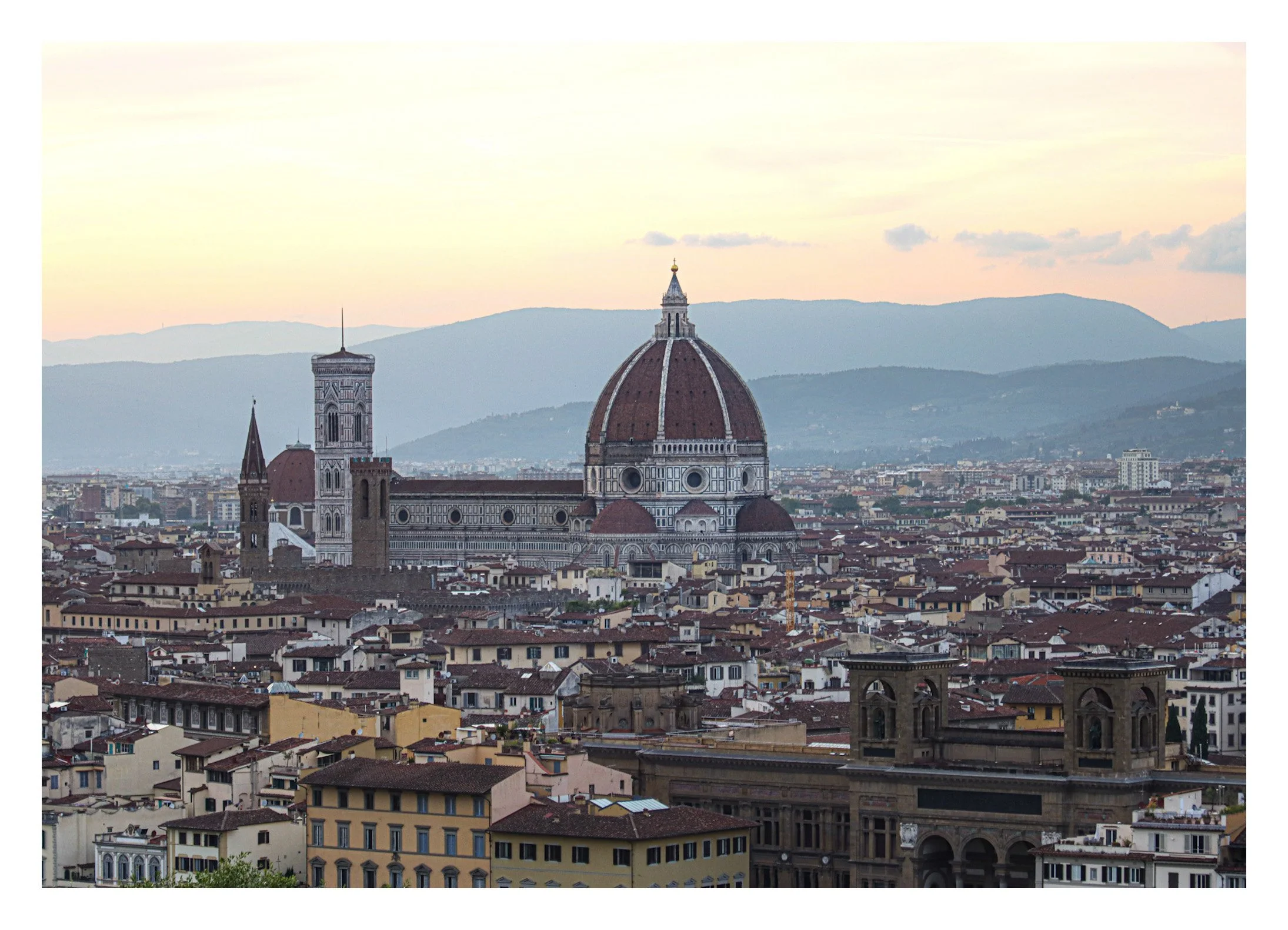 Panoramic view of Florence, Italy, featuring the Florence Cathedral with its large dome and bell tower, surrounded by city buildings and distant mountains.