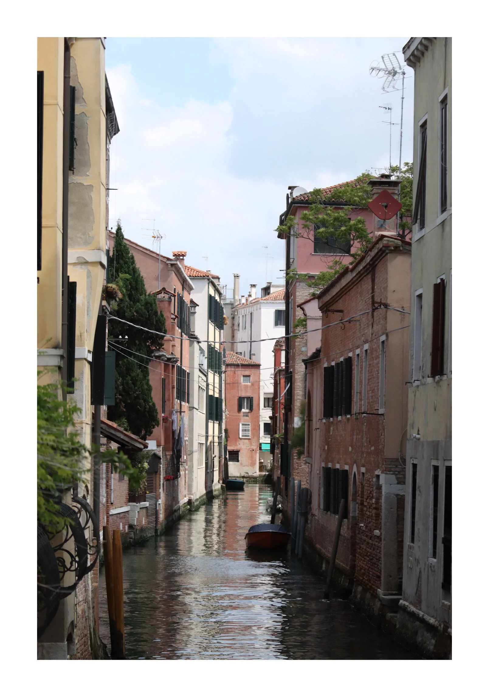 A narrow canal lined with colorful old buildings on either side, with a small boat floating on the water in Venice, Italy.