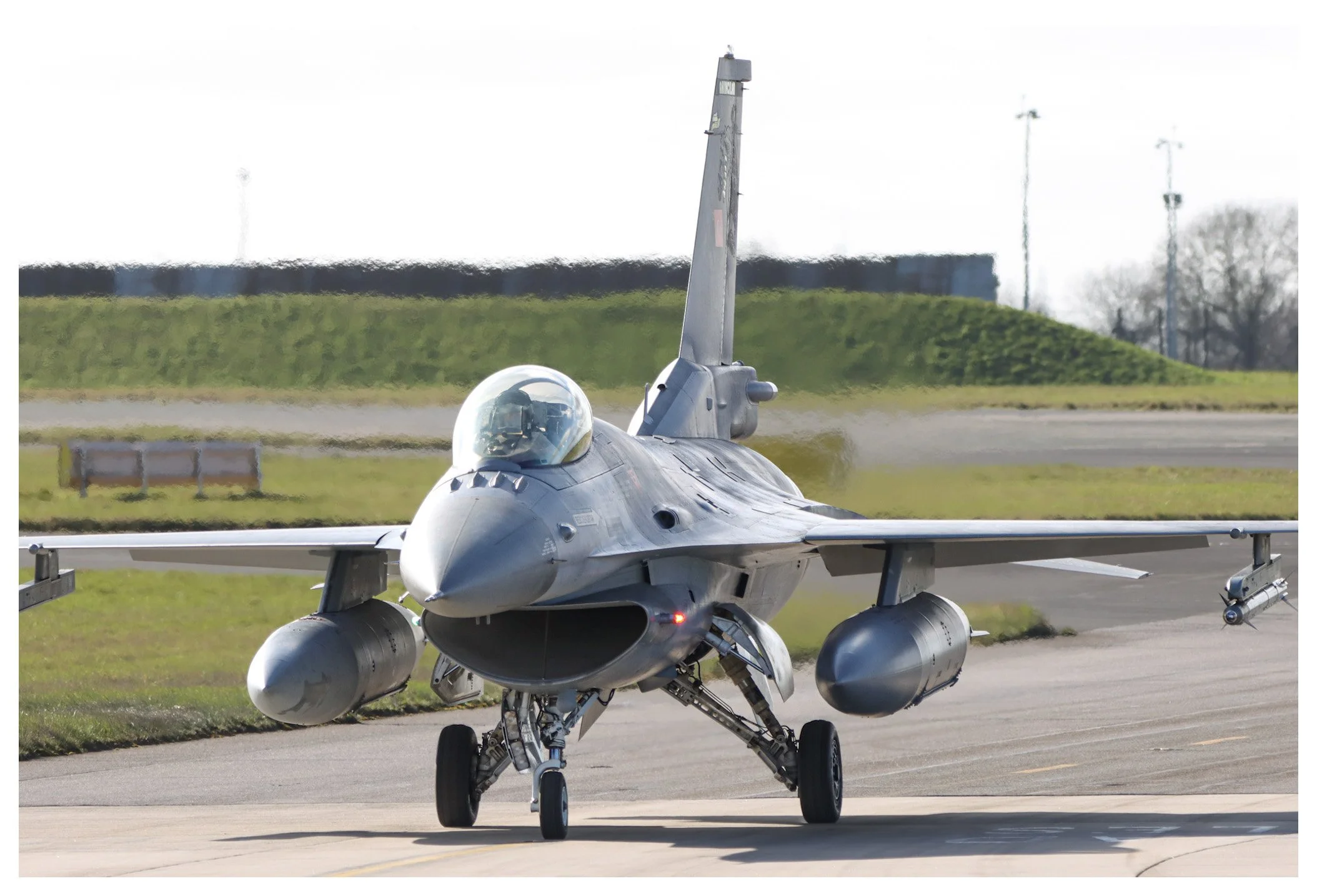 Front view of a fighter jet on the runway with its landing gear down, missile under the wing, and appears ready for flight.