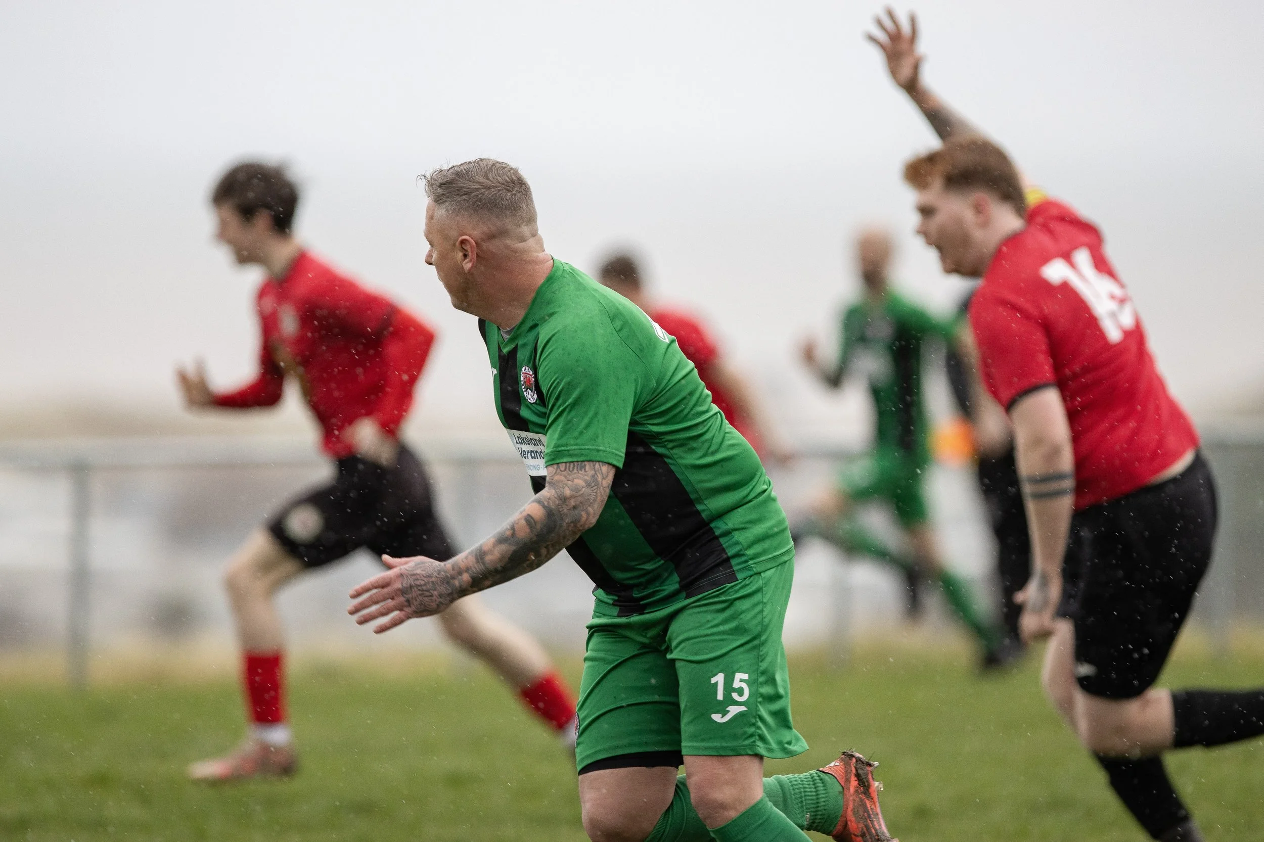 Soccer players running on the field during a game, with the player in the foreground wearing a green jersey with the number 15.