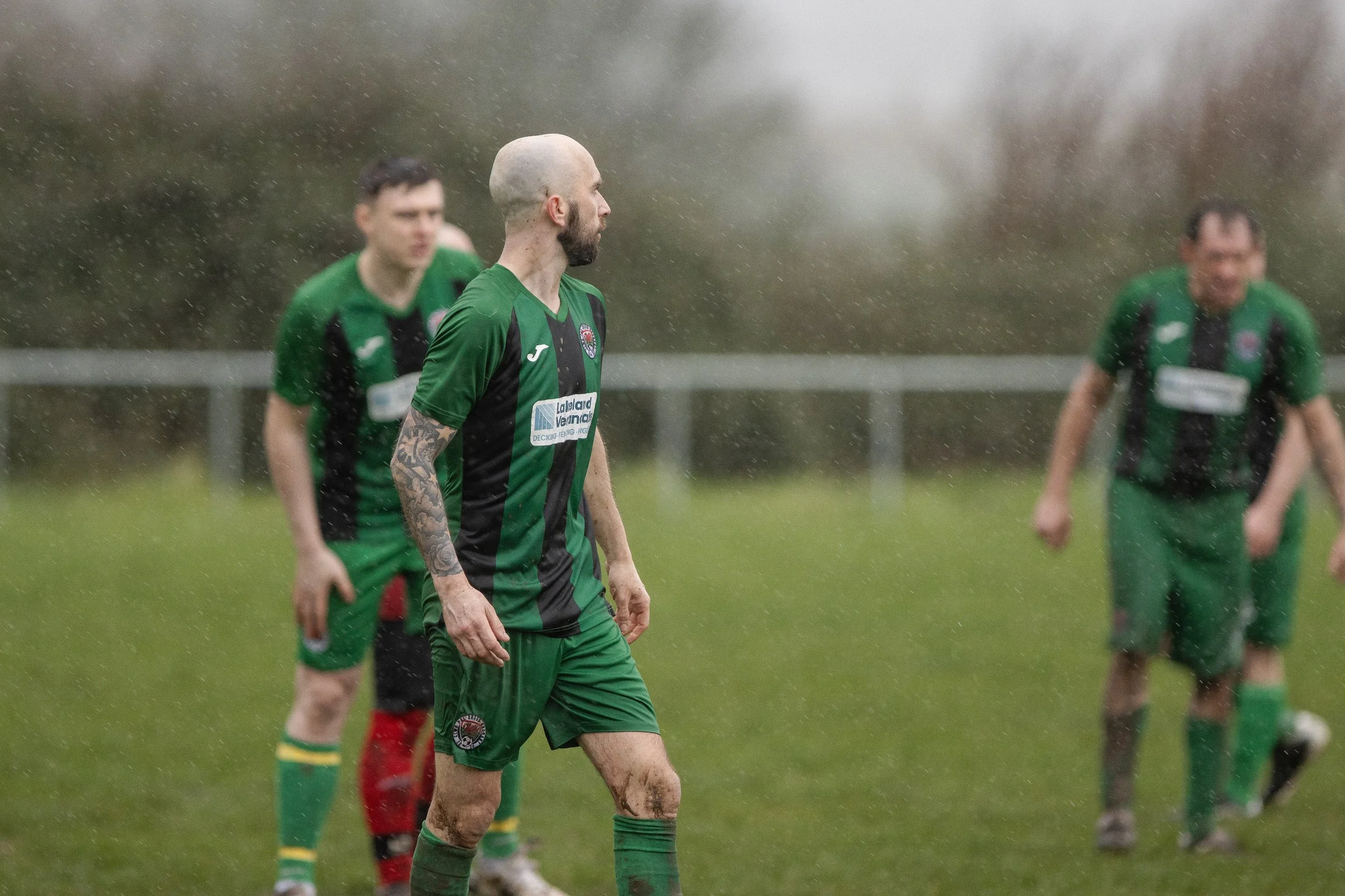 Soccer players on the field in rainy weather, wearing green and black uniforms.