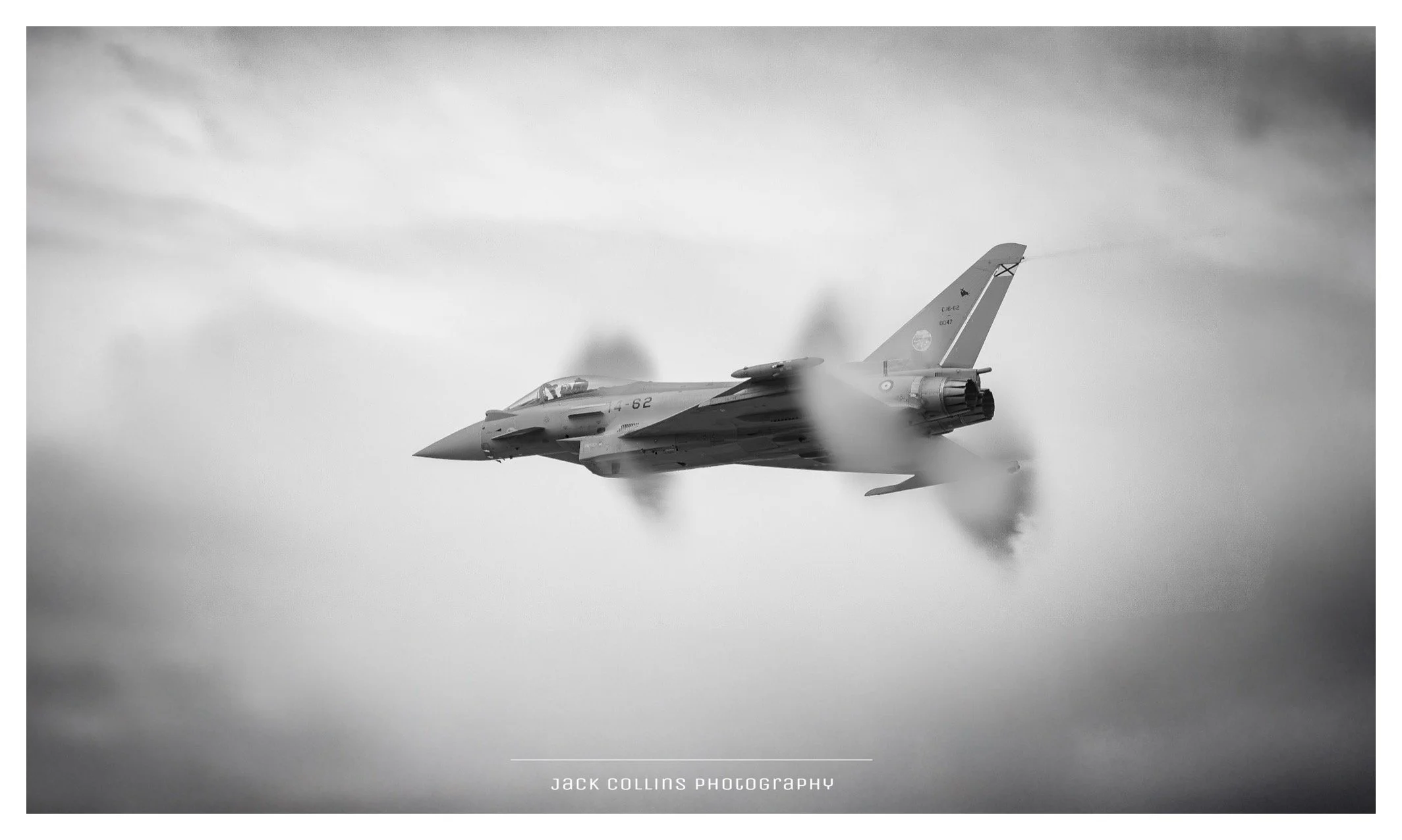 A jet fighter flying through the sky with vapor trails and clouds, captured in black and white.
