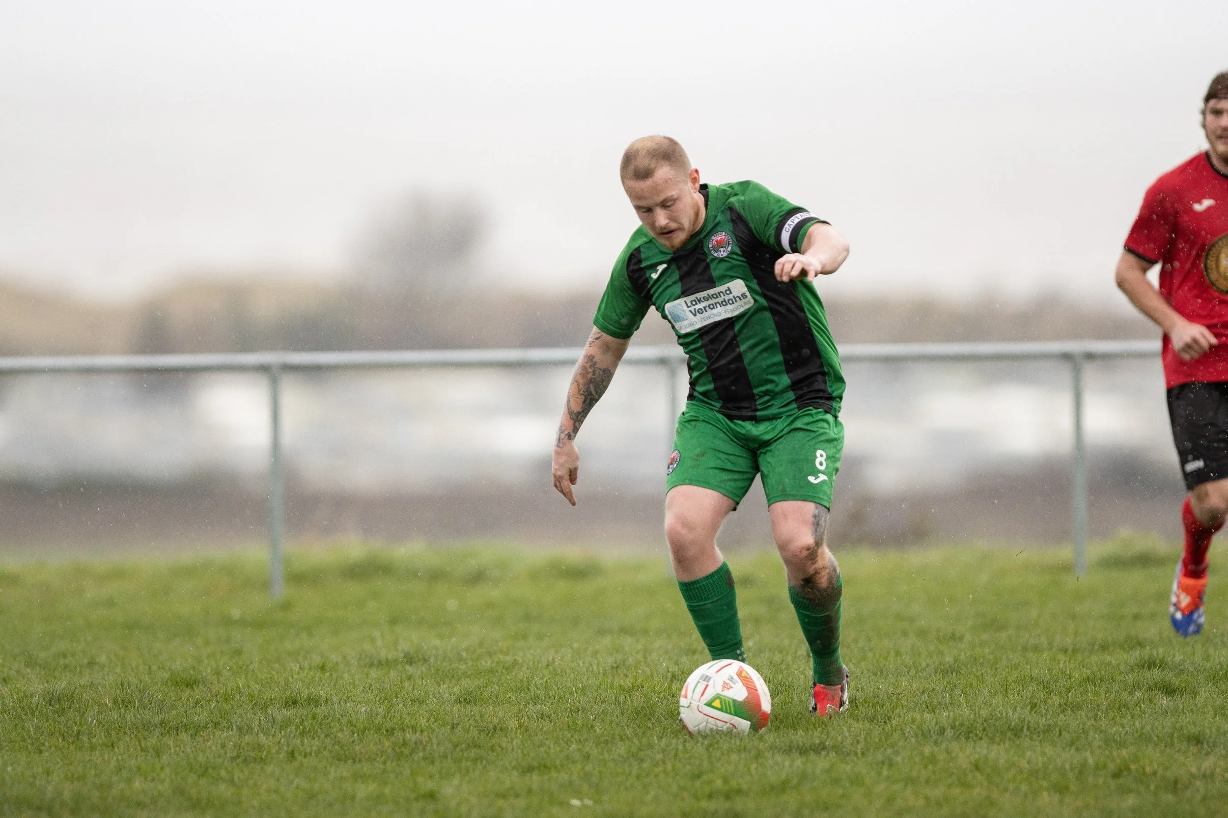 A soccer player in a green and black uniform is about to kick a white and green soccer ball on a grassy field.