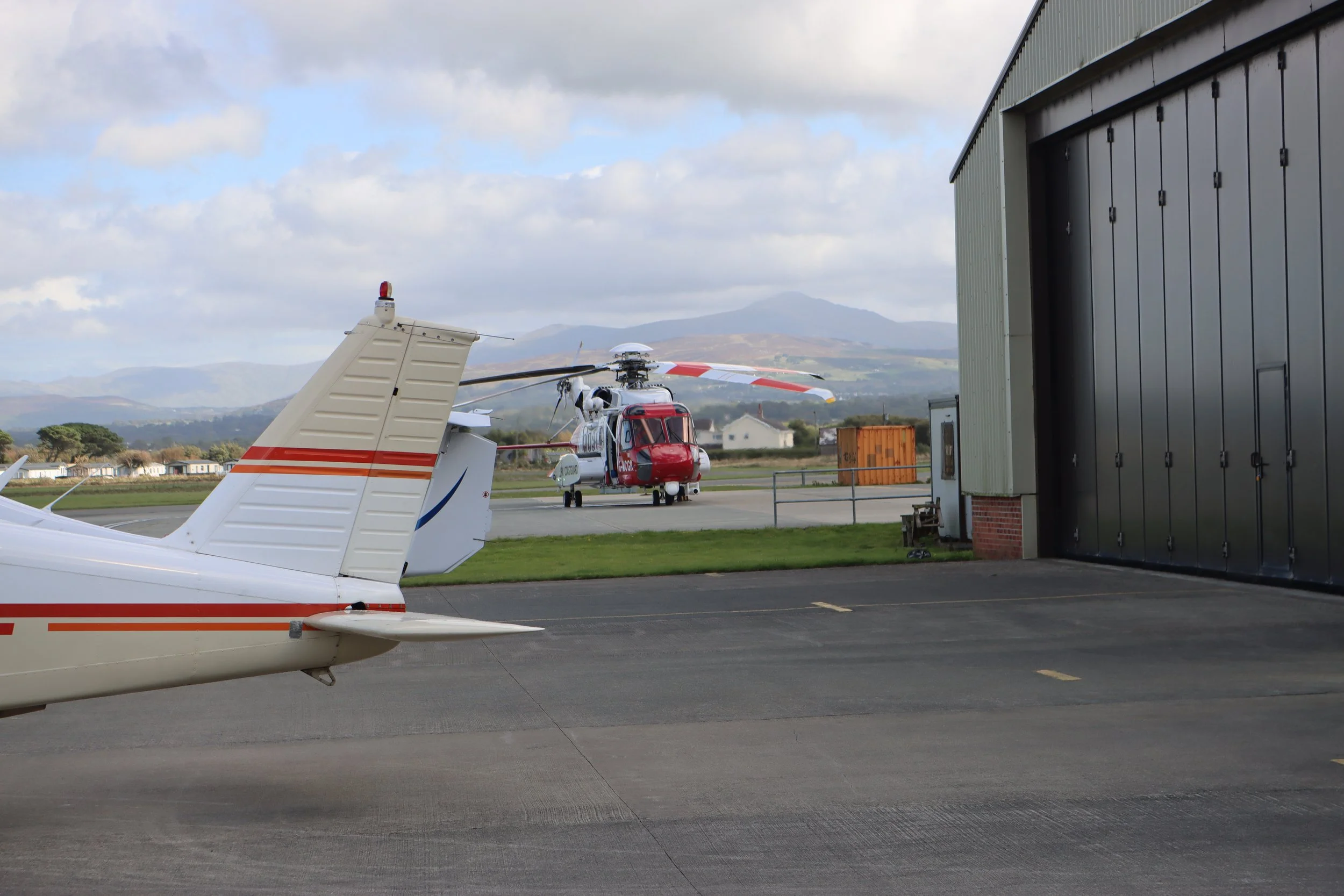 Helicopter on the tarmac near a hangar with mountainous landscape in the background.