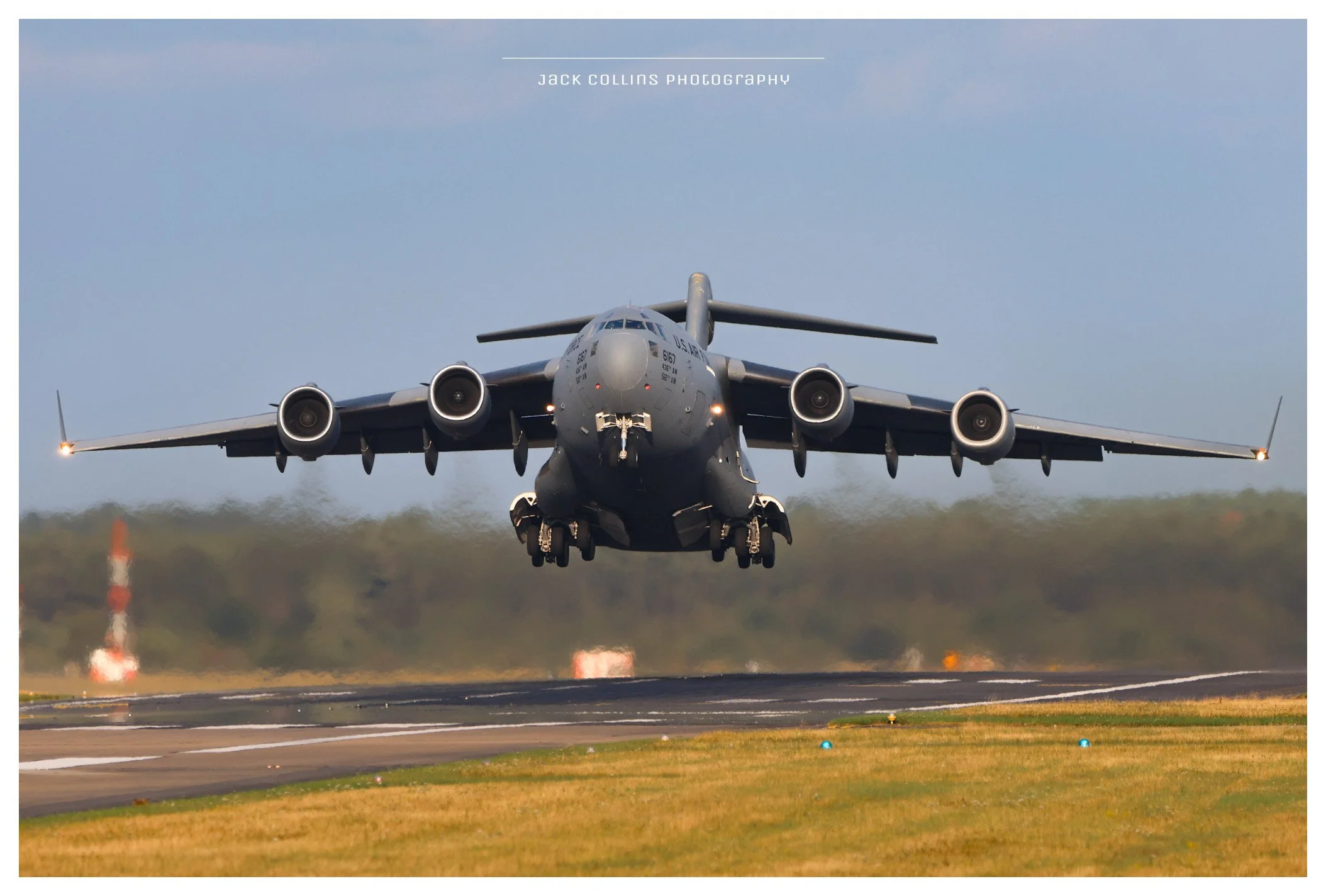 Military cargo plane taking off from runway, with its wheels still in contact with the ground.