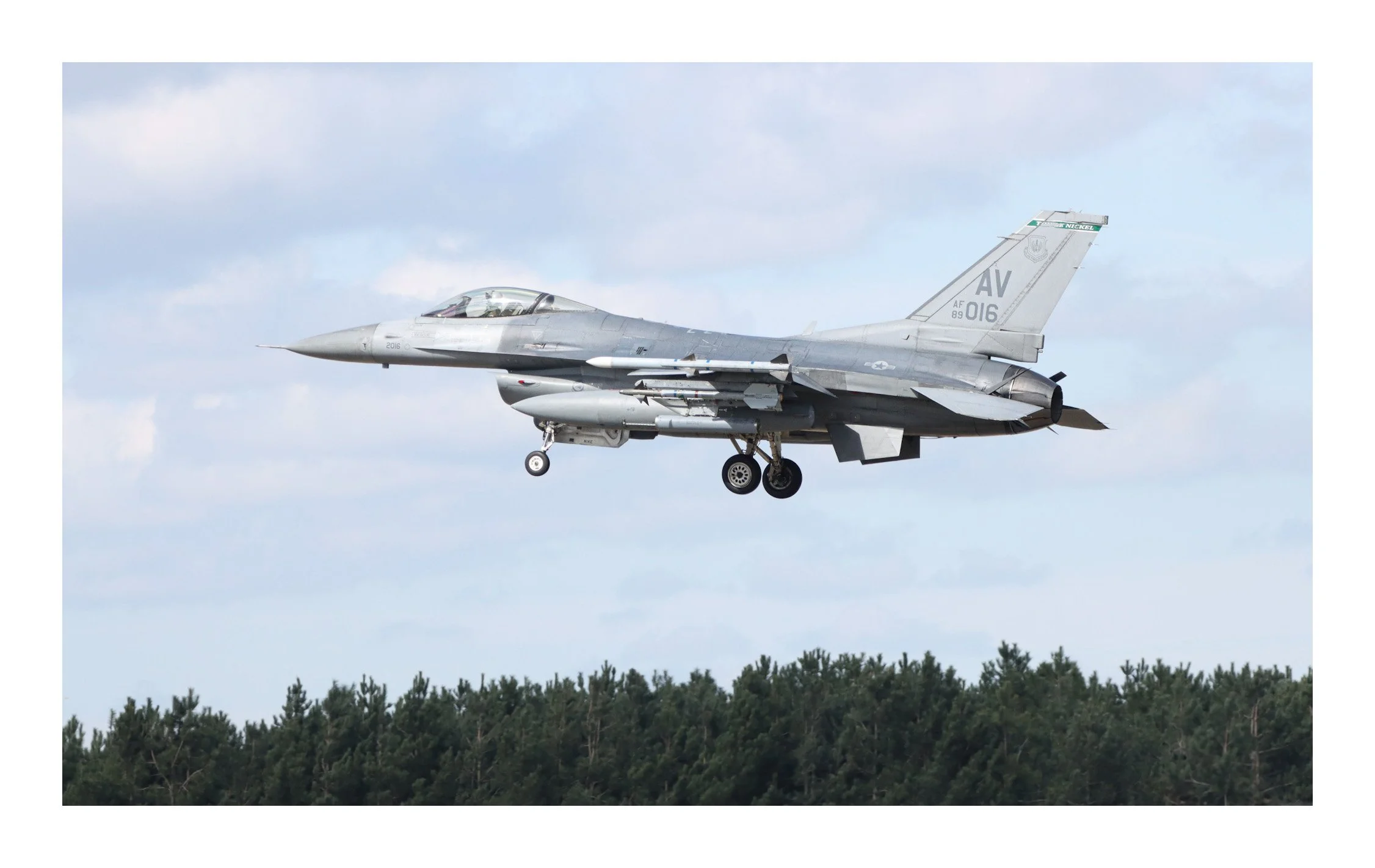 A gray fighter jet aircraft flying low over a forested area during daytime.