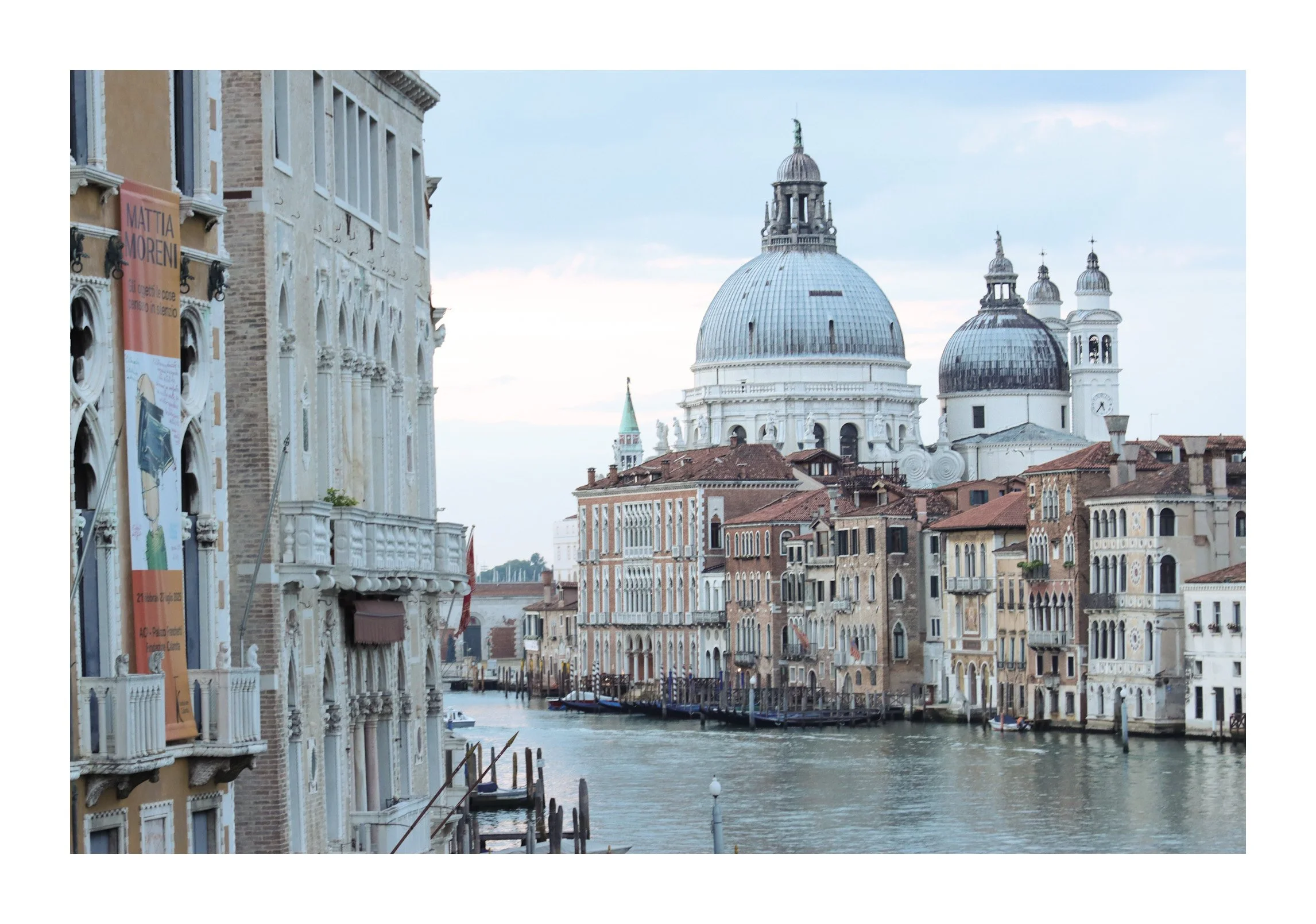 View of Venice canal with historic buildings, including domed churches, along the water, under a cloudy sky.