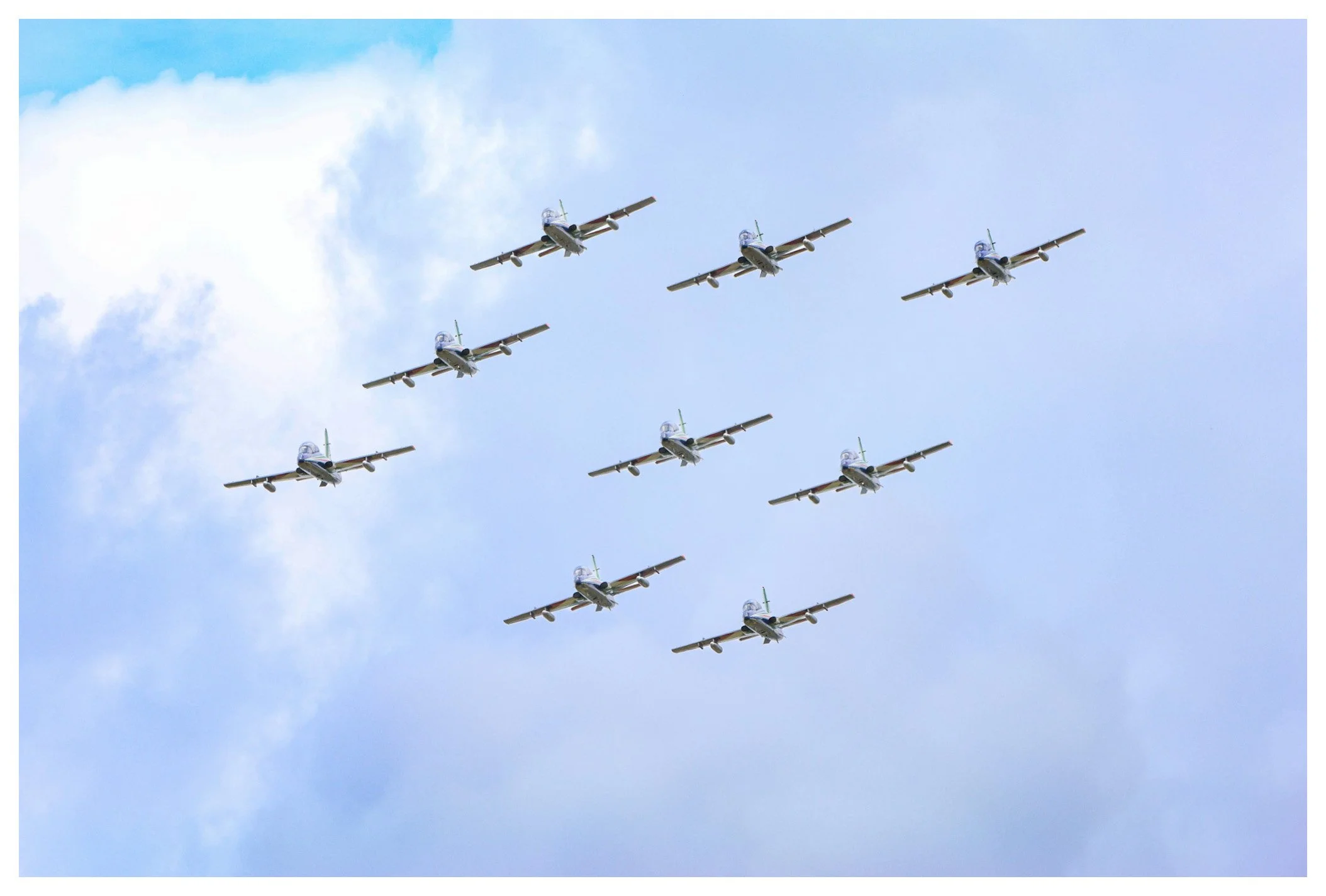 Six vintage fighter jets flying in formation against a blue sky with scattered clouds.
