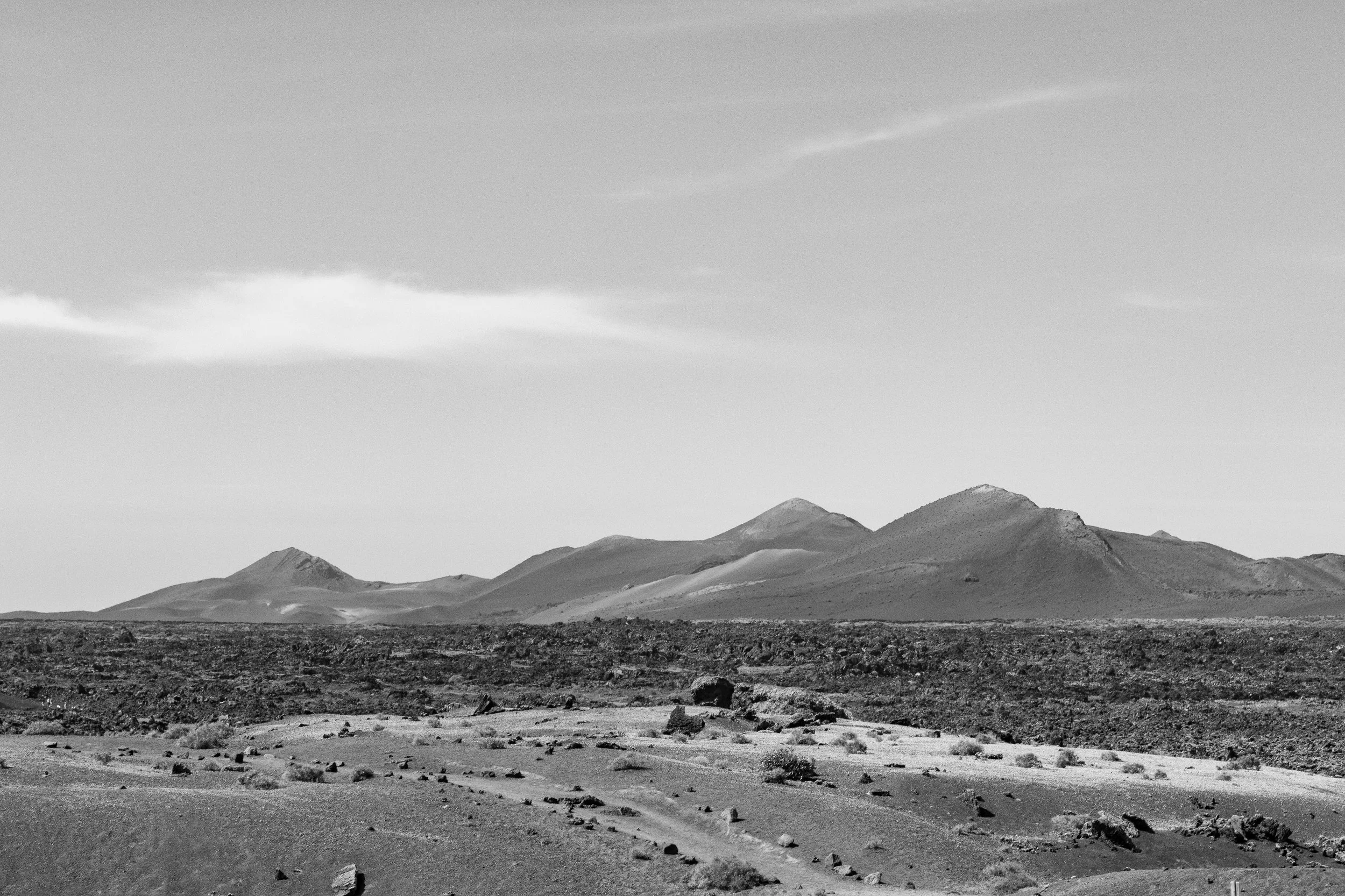 A black-and-white photo of a vast desert landscape with rocky terrain and distant mountains under a partly cloudy sky.