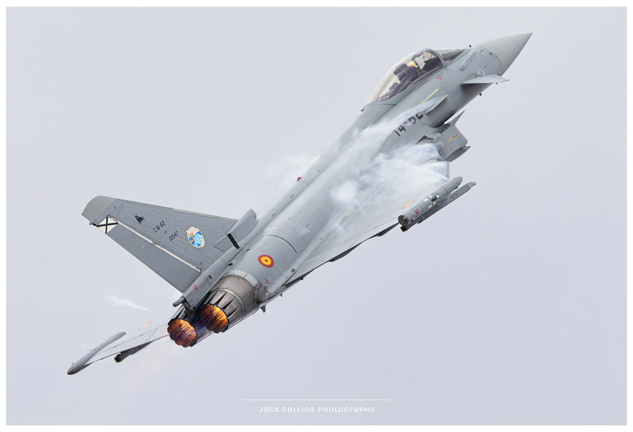 Photo of eurofighter jet aircraft in flight, with afterburners lit, tilted upward against a cloudy sky.