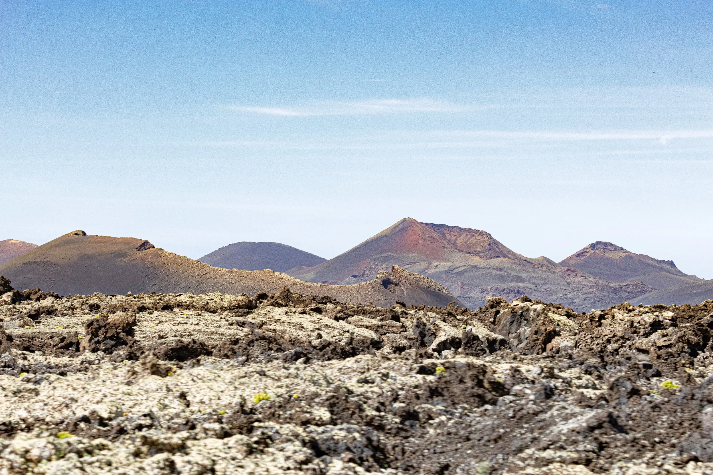 Scenic view of volcanic landscape with multiple dark, rocky mountain peaks under a blue sky.
