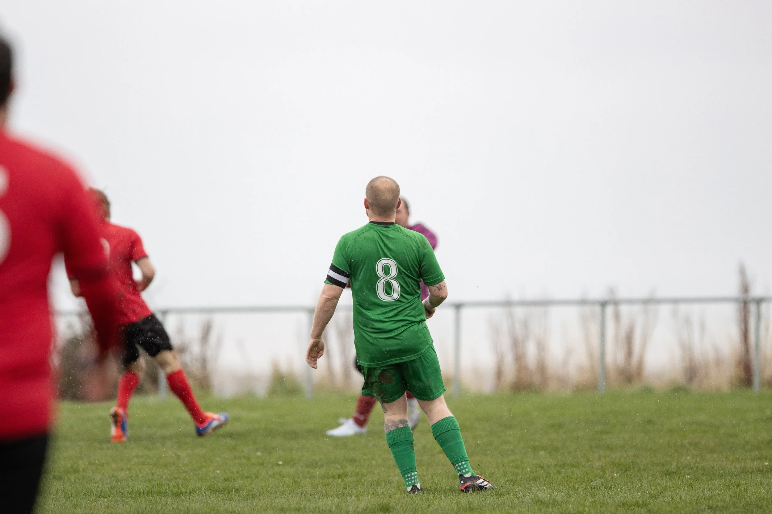 Soccer players on a field during a match with foggy weather, one in a green jersey with the number 8, and others in red jerseys.