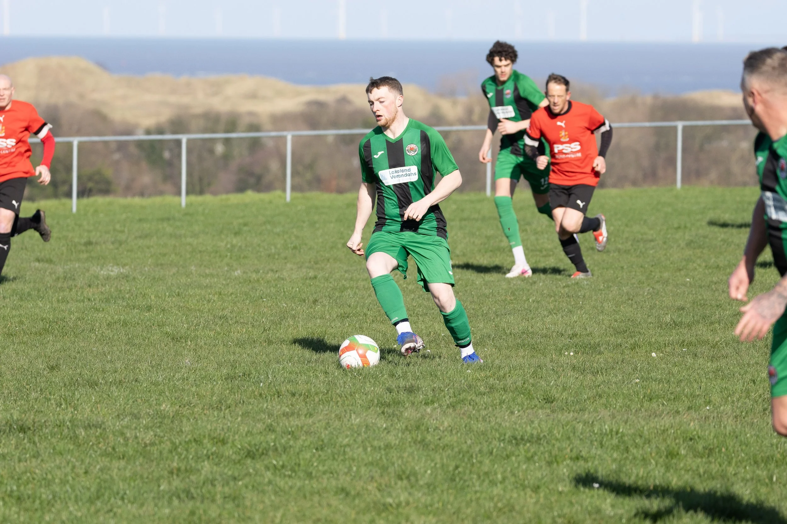 Soccer players in green and red uniforms playing on a grassy field during daytime.