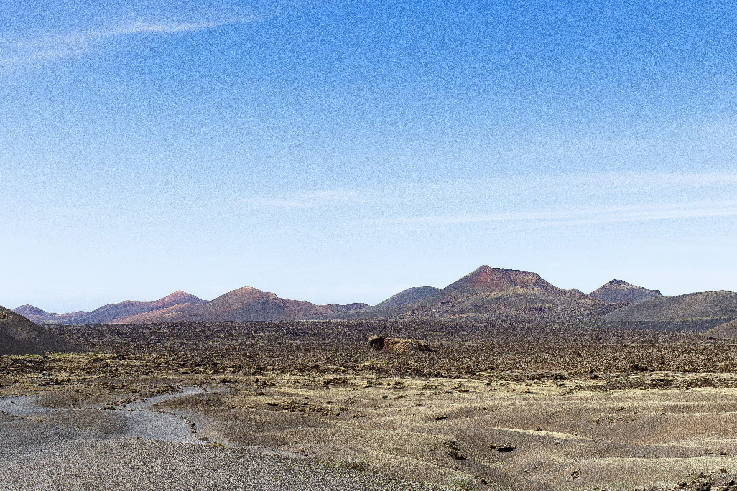 Desert landscape with rocky terrain and mountain ranges in the distance under a clear blue sky.