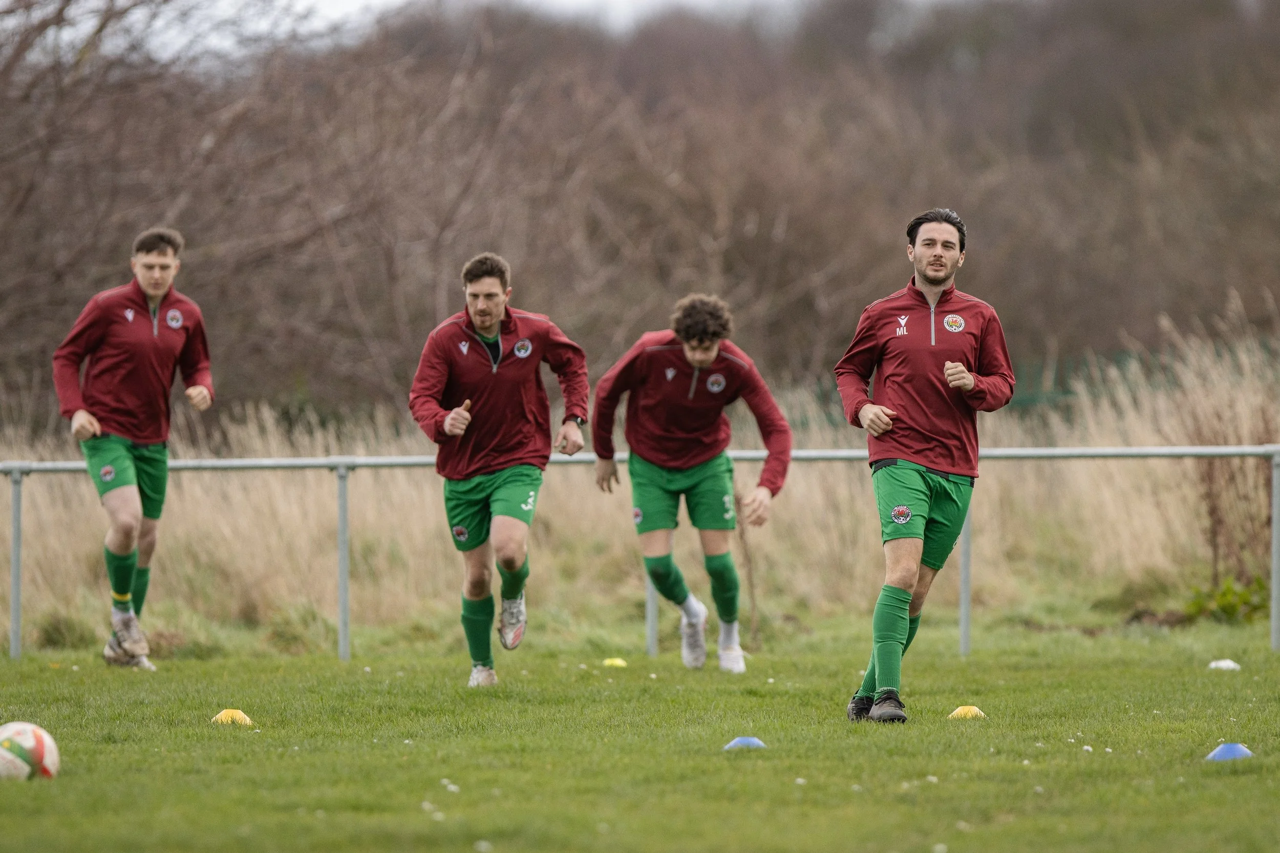 Four male soccer players in matching red and green training gear running on a field during practice.
